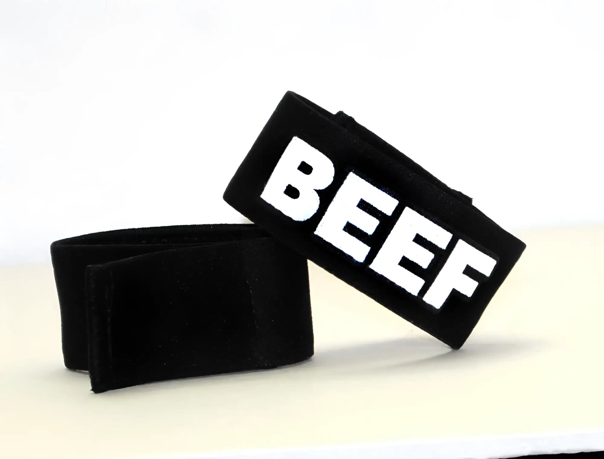 Two black fabric adjustable bands, one with "BEEF" in bold white lettering, against a plain white background.