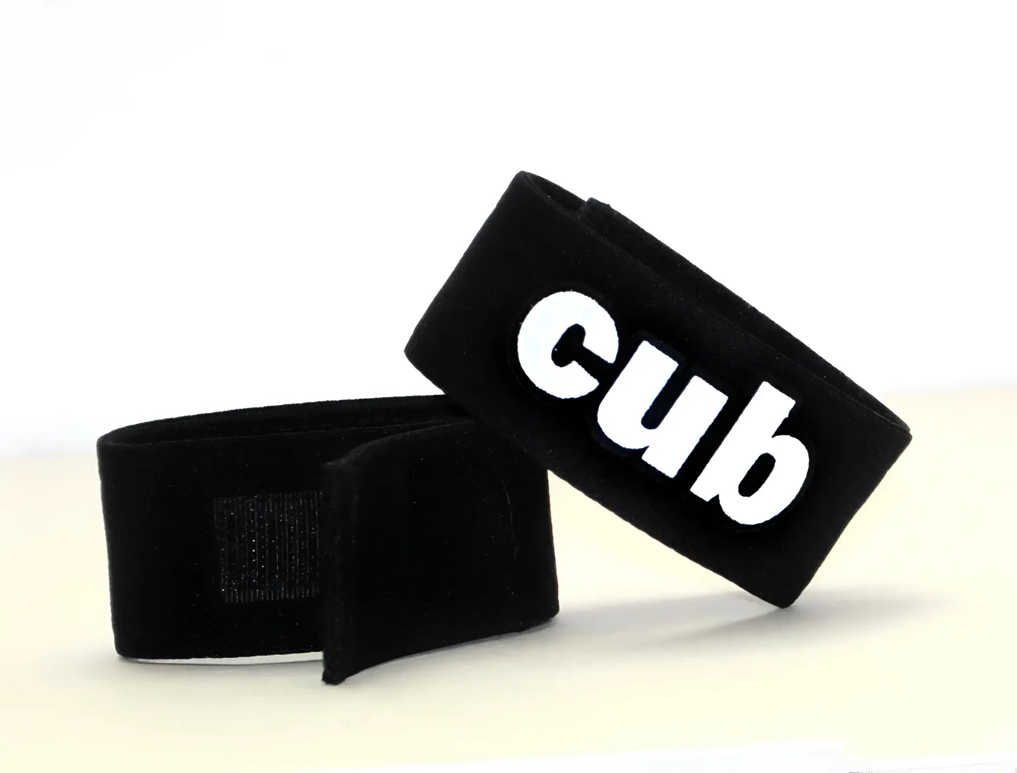 Two black adjustable fabric cock rings with "cub" embroidered in white lettering on one side and velcro closures.