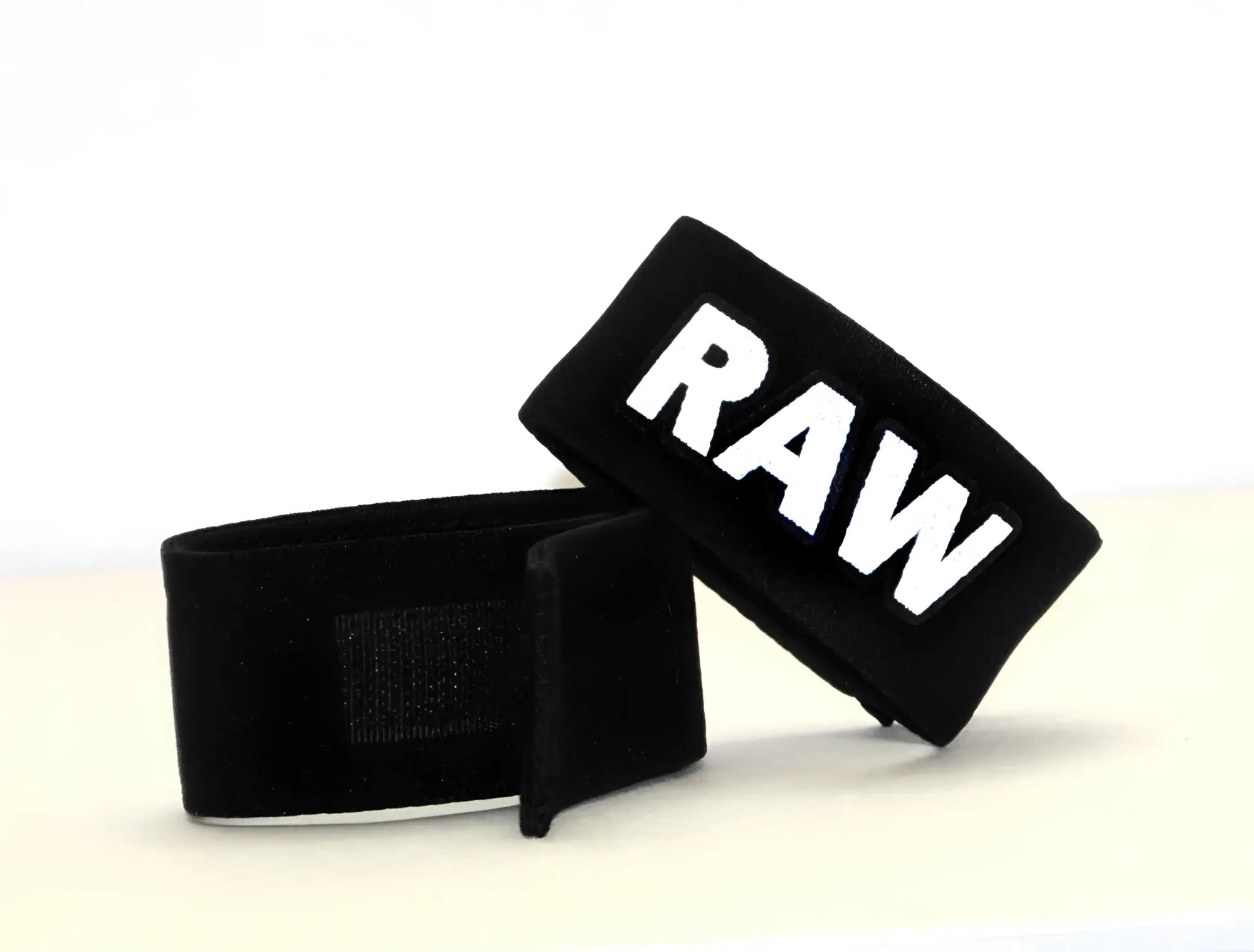 Two black, adjustable velcro cock rings with the word "RAW" stitched in bold white lettering.