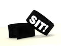 Two black fabric cock-ring bands with velcro closures, one featuring the white text "SIT!" on a white background.