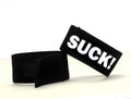 Black fabric cock ring with a Velcro closure and a white patch featuring the bold black text "SUCK!"