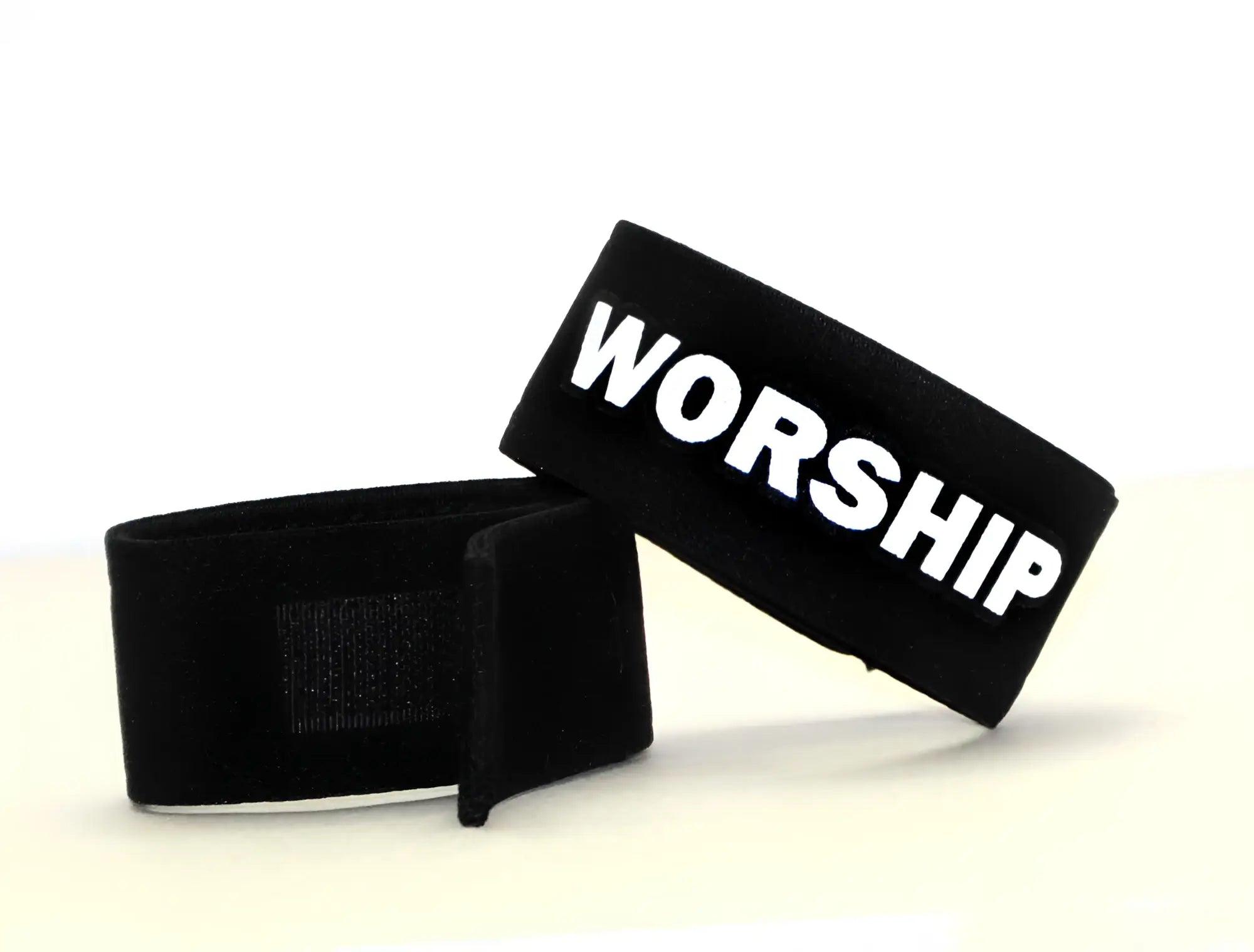 Two black fabric cock rings with adjustable velcro closures; one features the word "WORSHIP" in white bold letters.