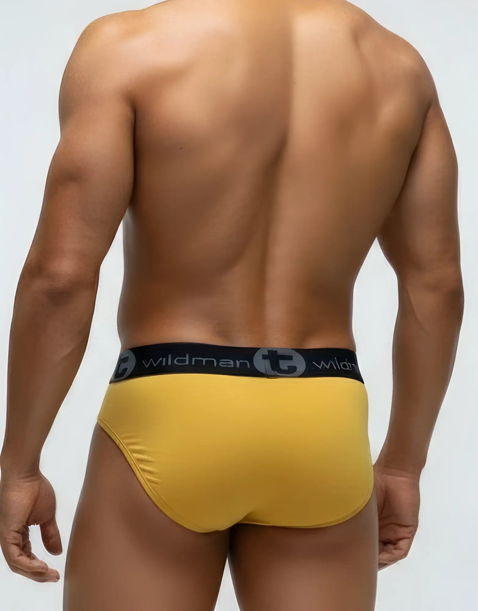 Muscular man wearing gold WildmanT modal pouch briefs with a black branded waistband, seen from behind.