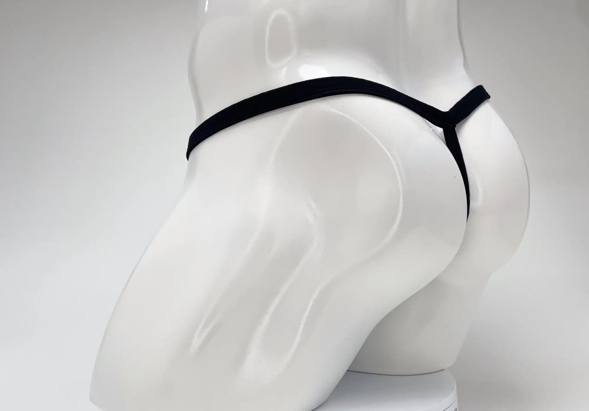 A black WildmanT thong shown from the rear on a glossy white male mannequin.