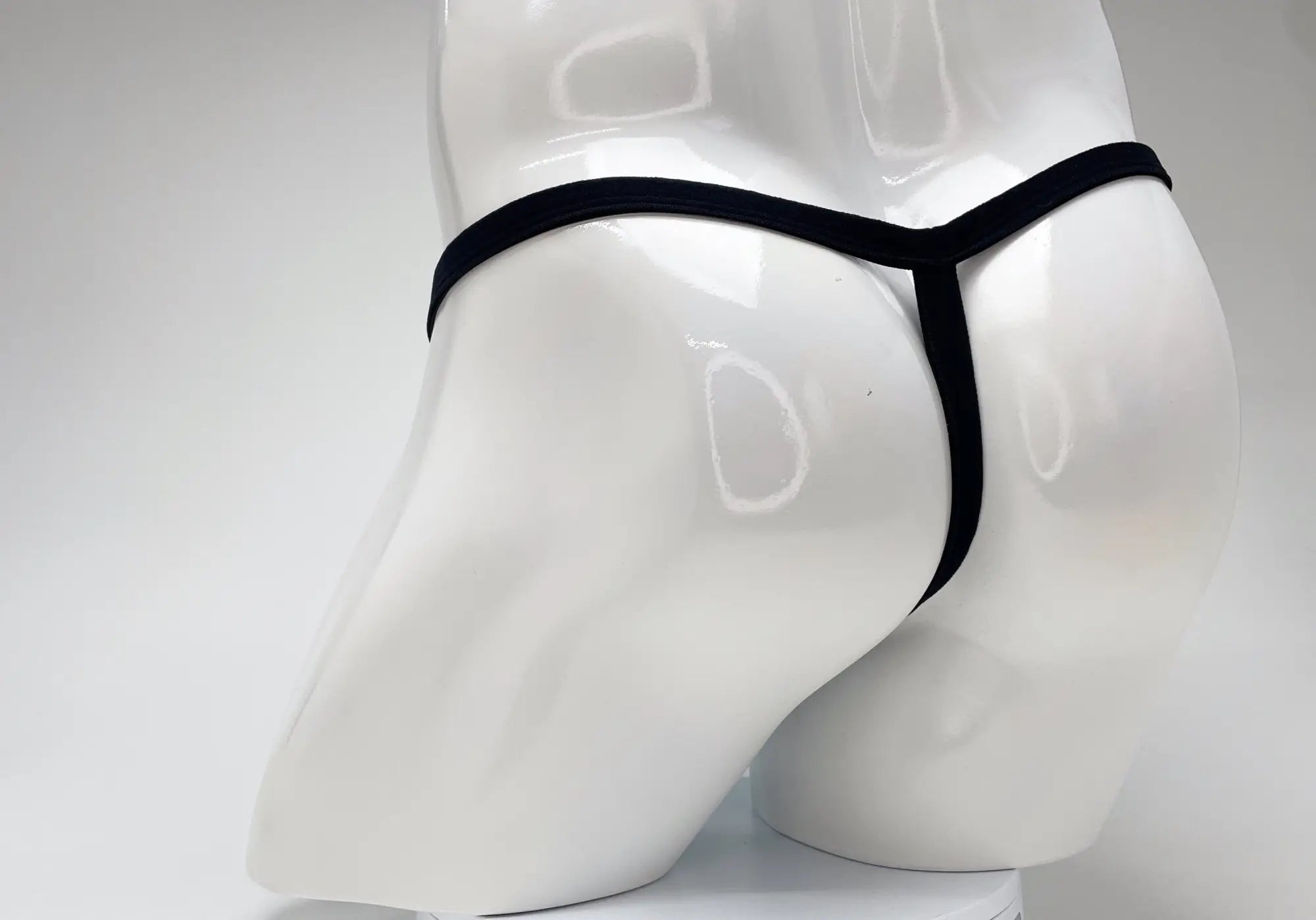 Black string thong on a glossy white male mannequin torso against a plain white background.