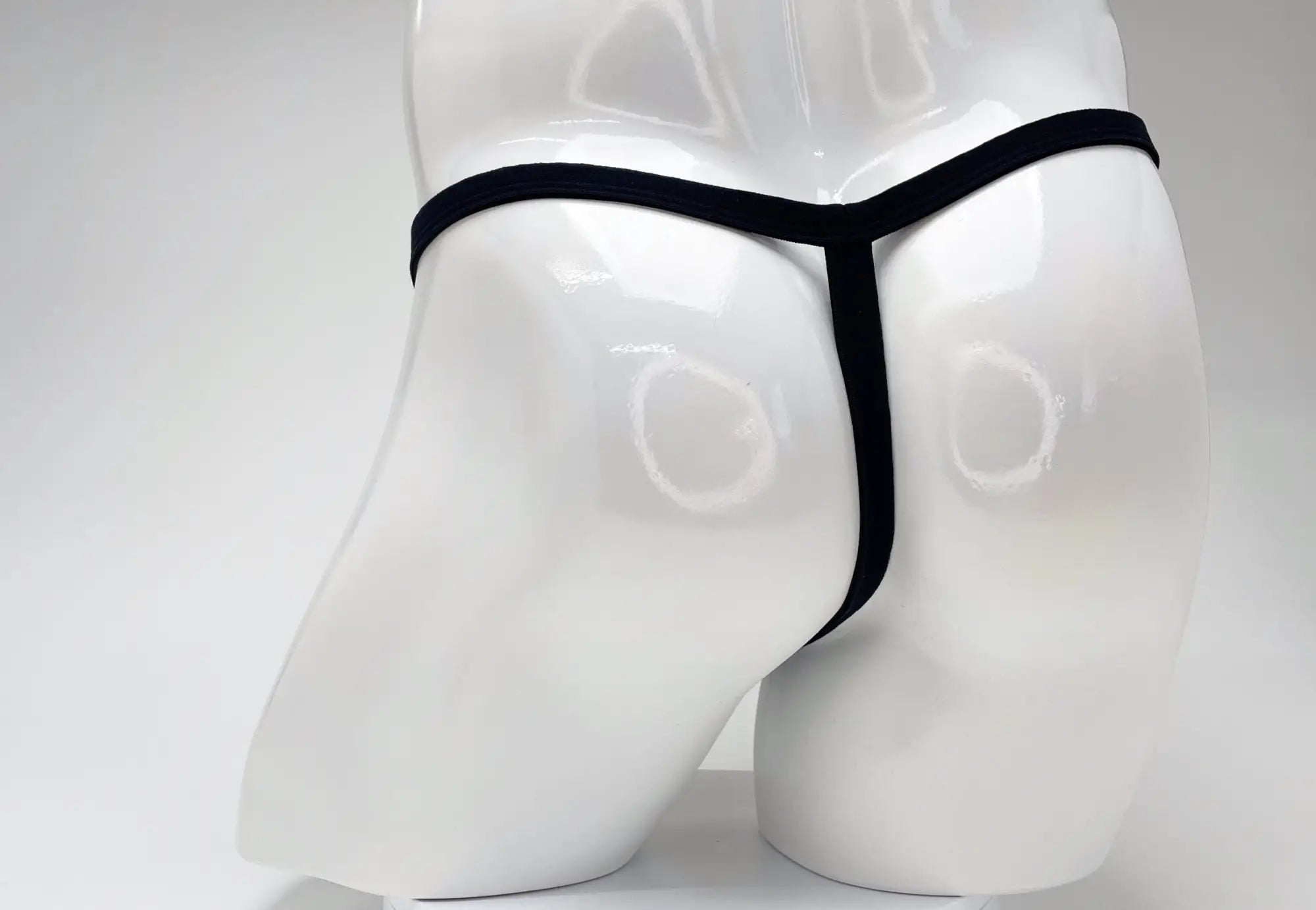 Back view of a black modal micro thong on a glossy white male mannequin torso.