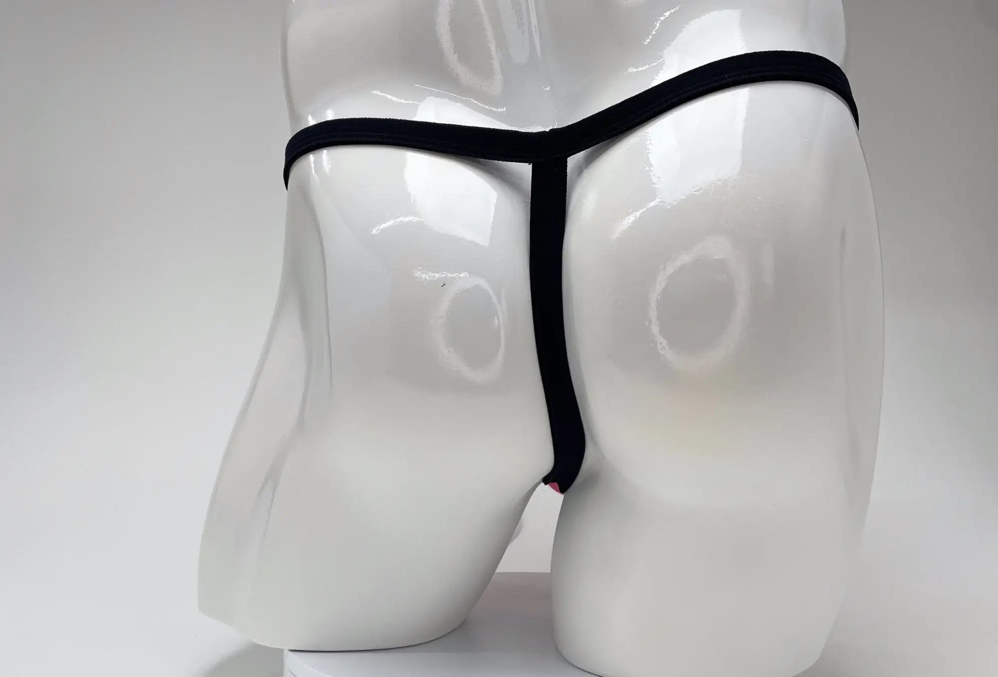 Back view of WildmanT micro thong with thin black straps on a white mannequin, showing a hint of pink fabric.
