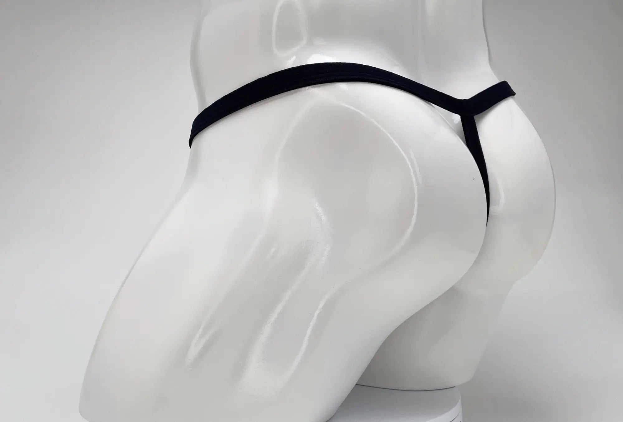 A black WildmanT micro thong with thin straps shown from behind on a white mannequin torso.