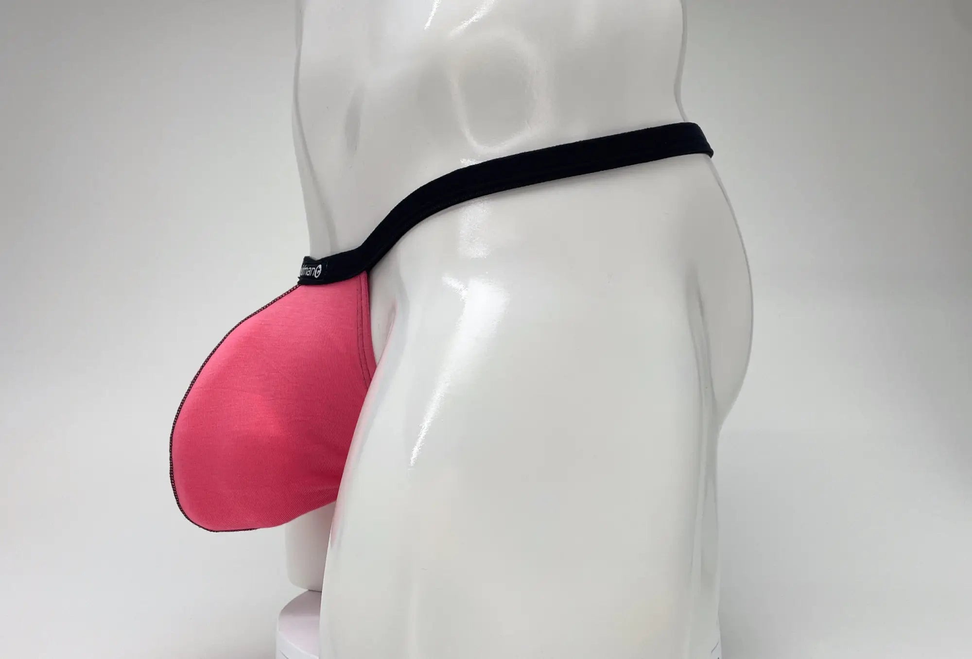 Pink WildmanT modal micro thong with a large pouch and black waistband on a white mannequin.