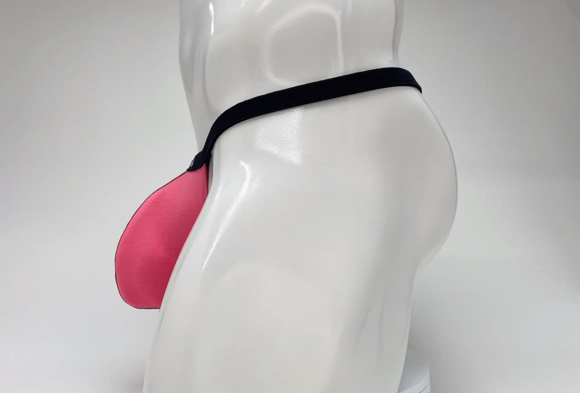 Side view of a bright pink modal micro thong with a large pouch and thin black waistband on a white mannequin.