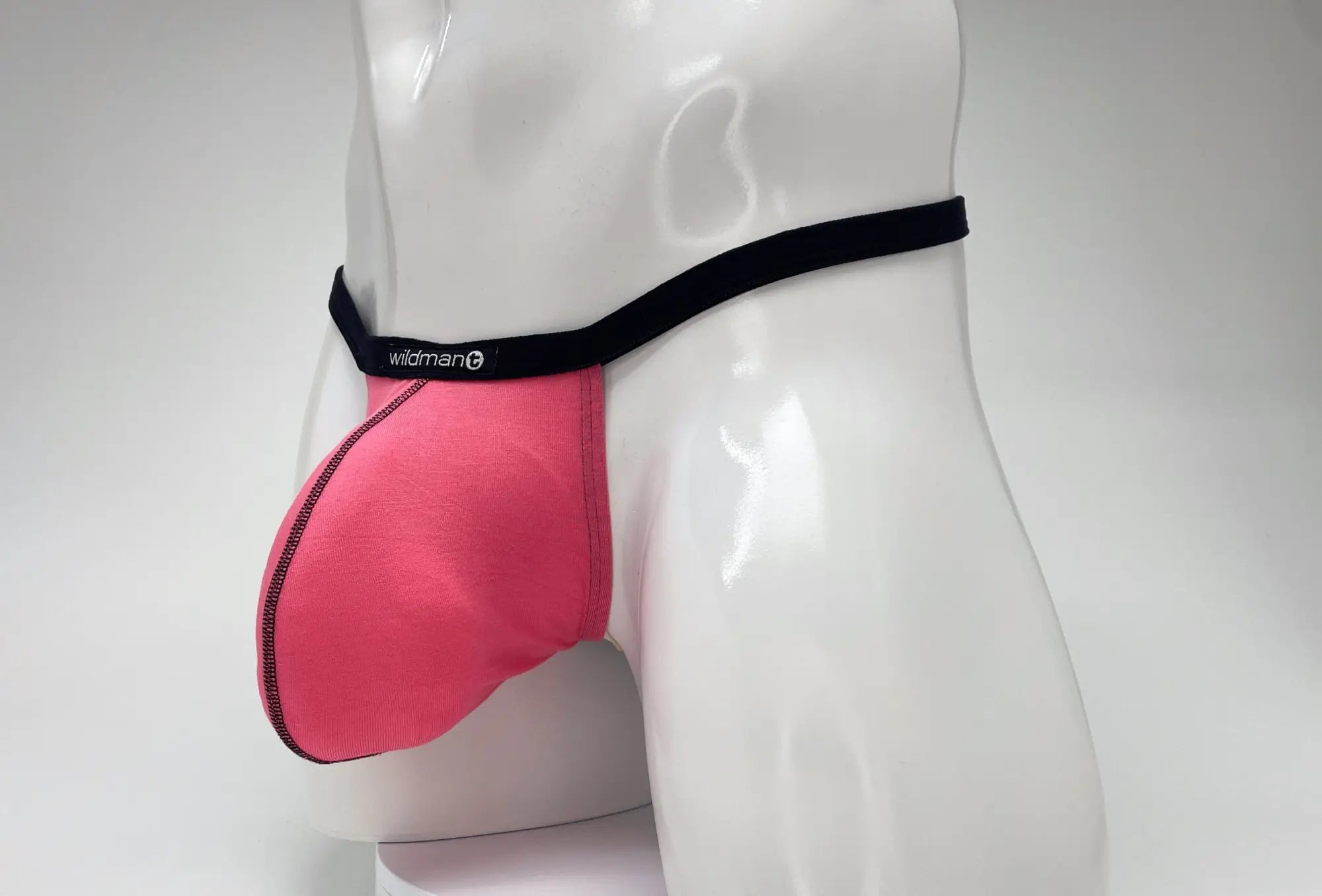 WildmanT pink modal micro thong with a prominent big boy pouch and black branded waistband on a mannequin torso.