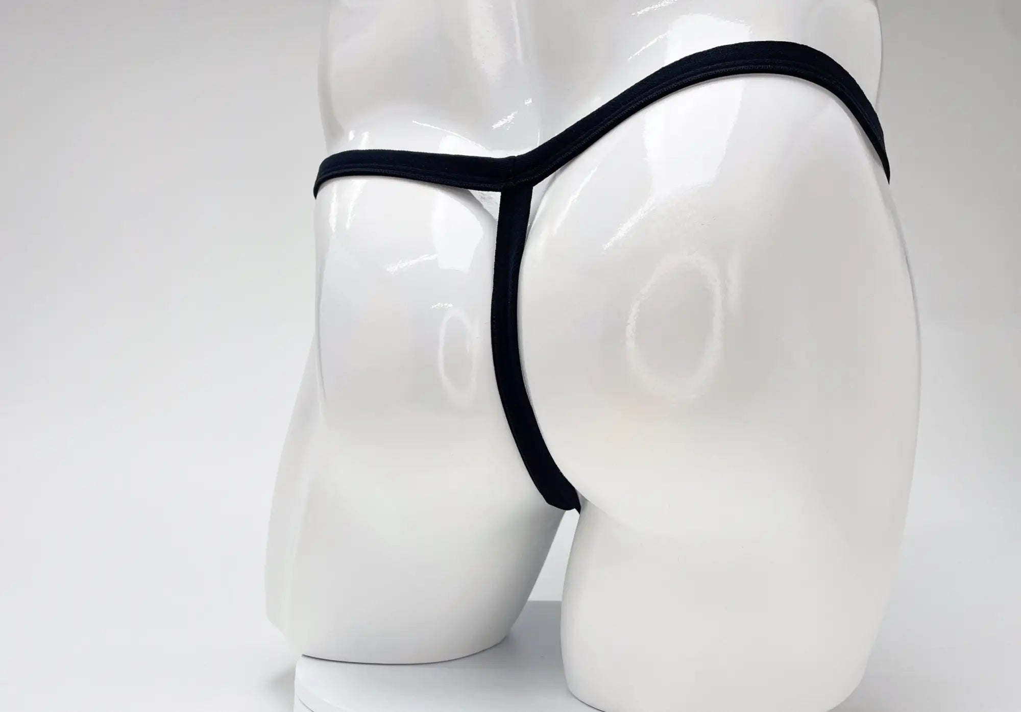 Back view of a black thong on a white mannequin torso, showing the thin elastic waistband and vertical rear strap.