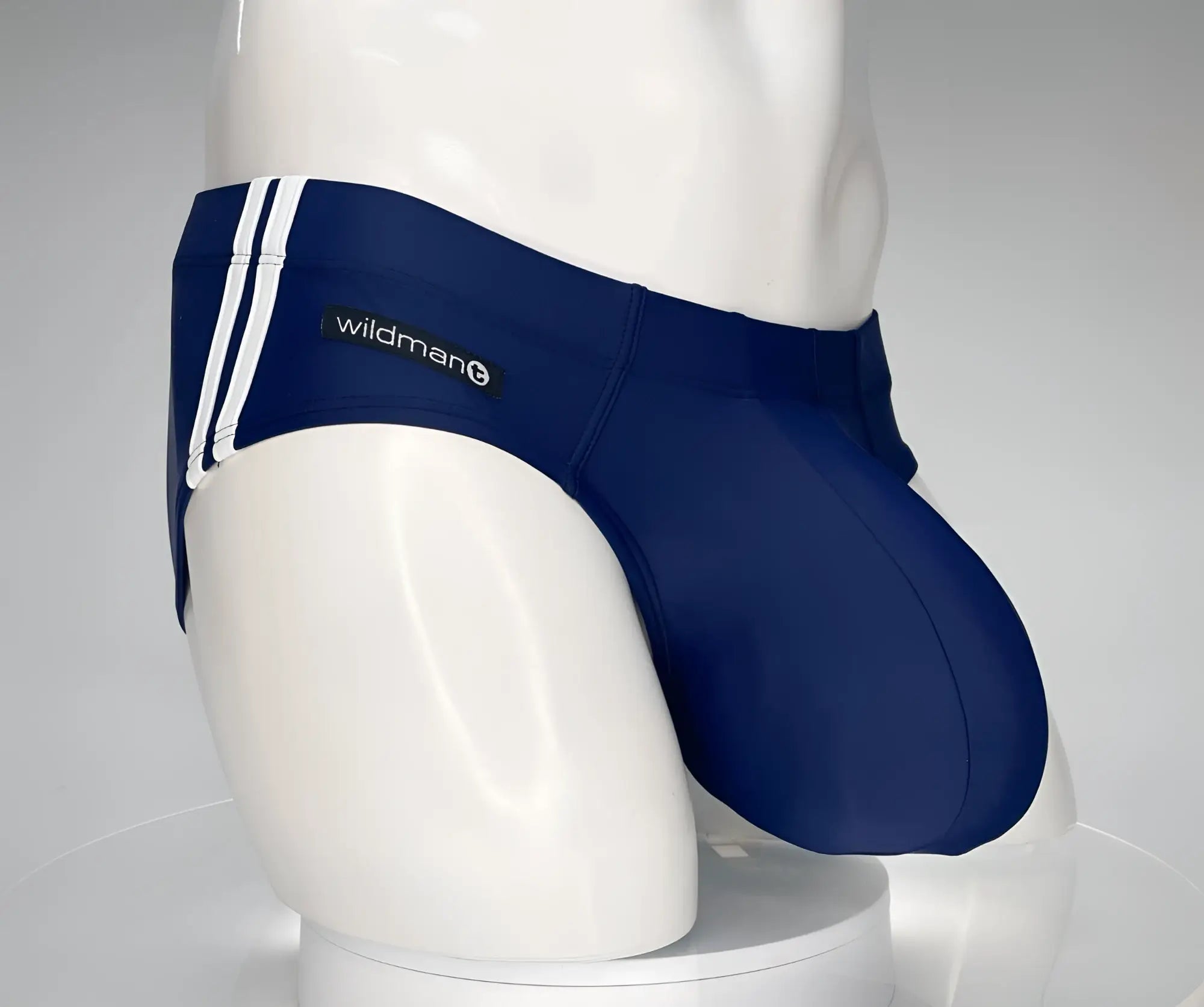 Navy blue WildmanT swim brief with a large pouch, white side stripes, and a brand logo patch on a mannequin.