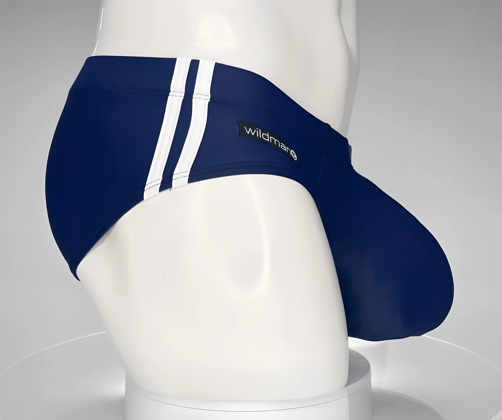Navy blue WildmanT swim brief with white side stripes and a branded tag, shown from a side profile on a mannequin.