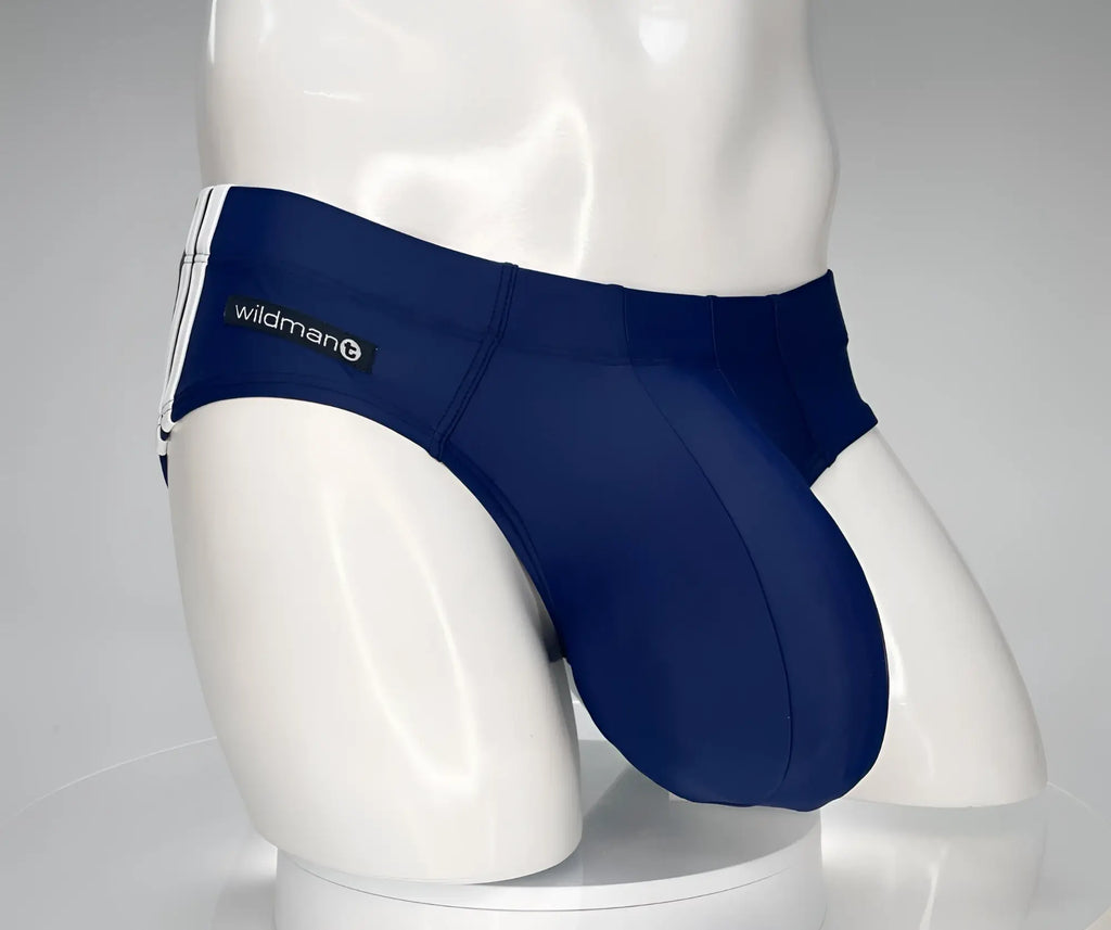 Navy blue WildmanT swim brief with contoured pouch, white side stripes, and a branded patch on a white mannequin.
