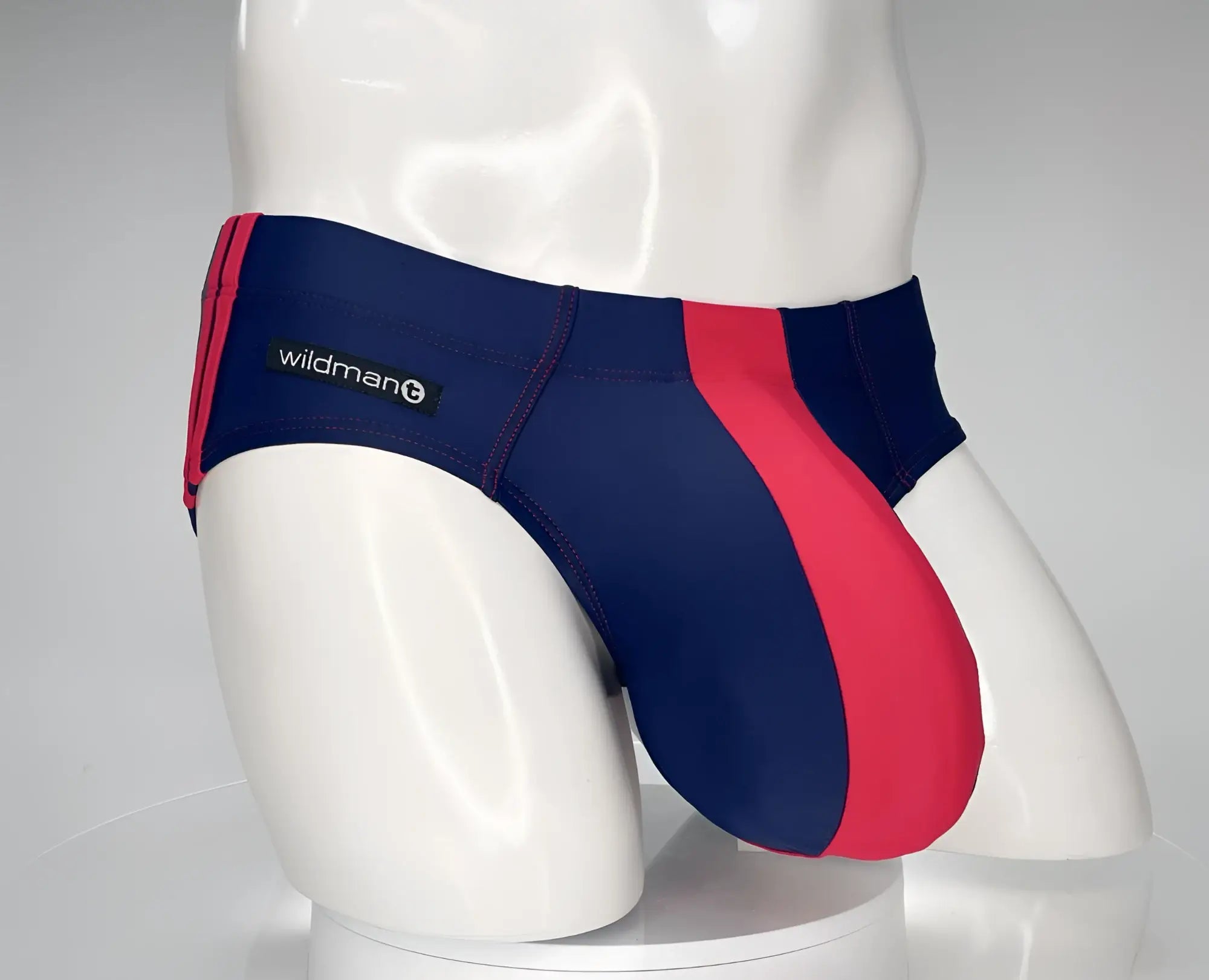 Navy and red WildmanT swim brief with a contoured pouch, red side panel, and side brand logo on a mannequin torso.