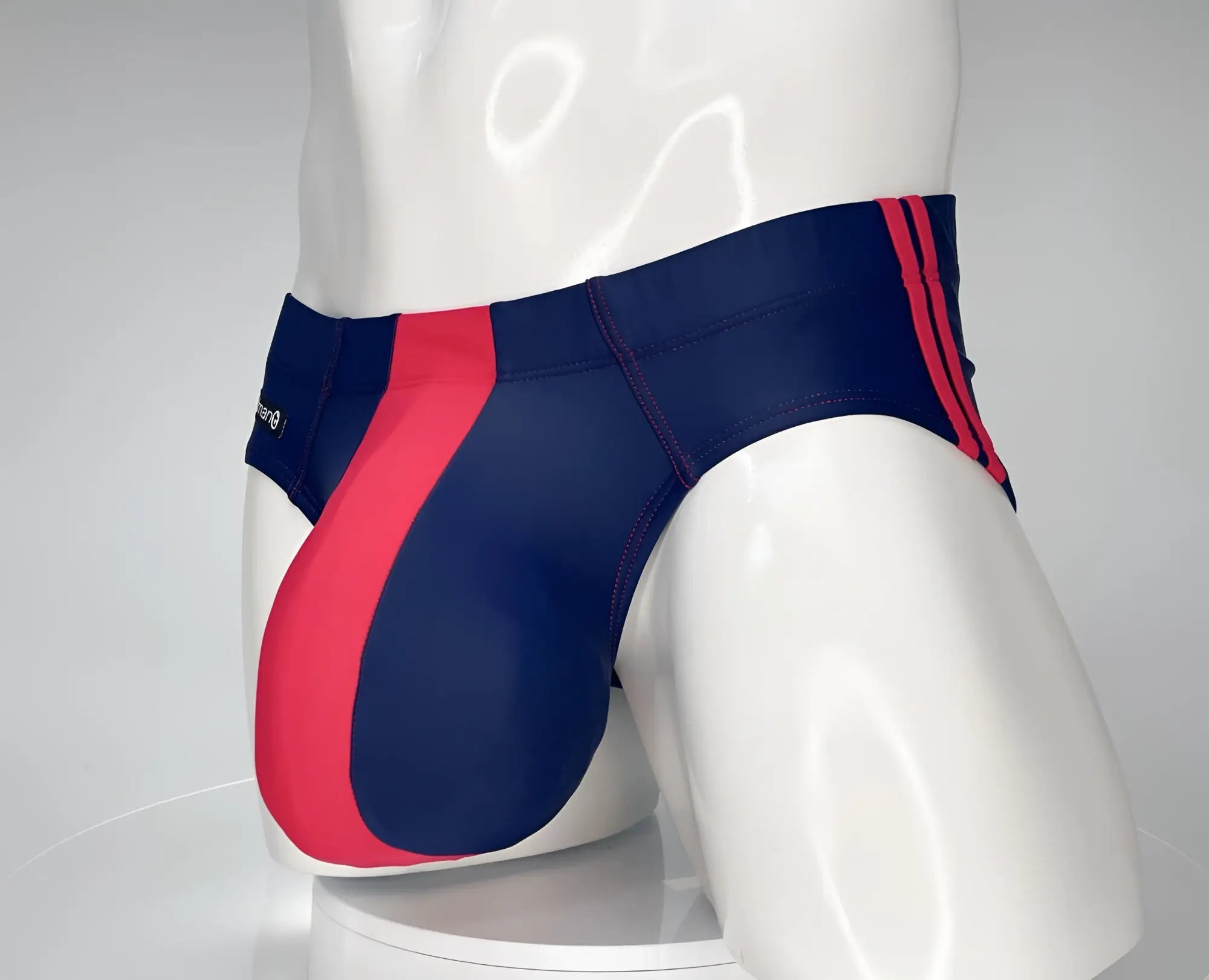 Navy blue swim brief with a prominent red front panel and red side stripes, worn on a white mannequin.