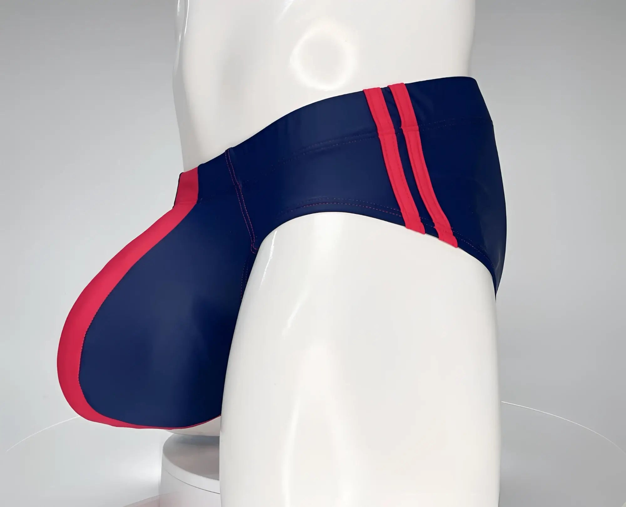 Navy blue and red swim brief with a contoured front pouch and double-stripe detail on a mannequin torso.