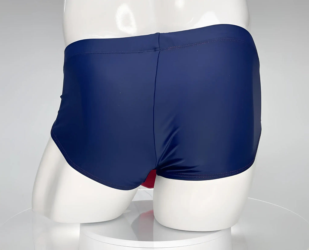 Back view of a navy blue WildmanT swim brief with red trim, modeled on a white mannequin.