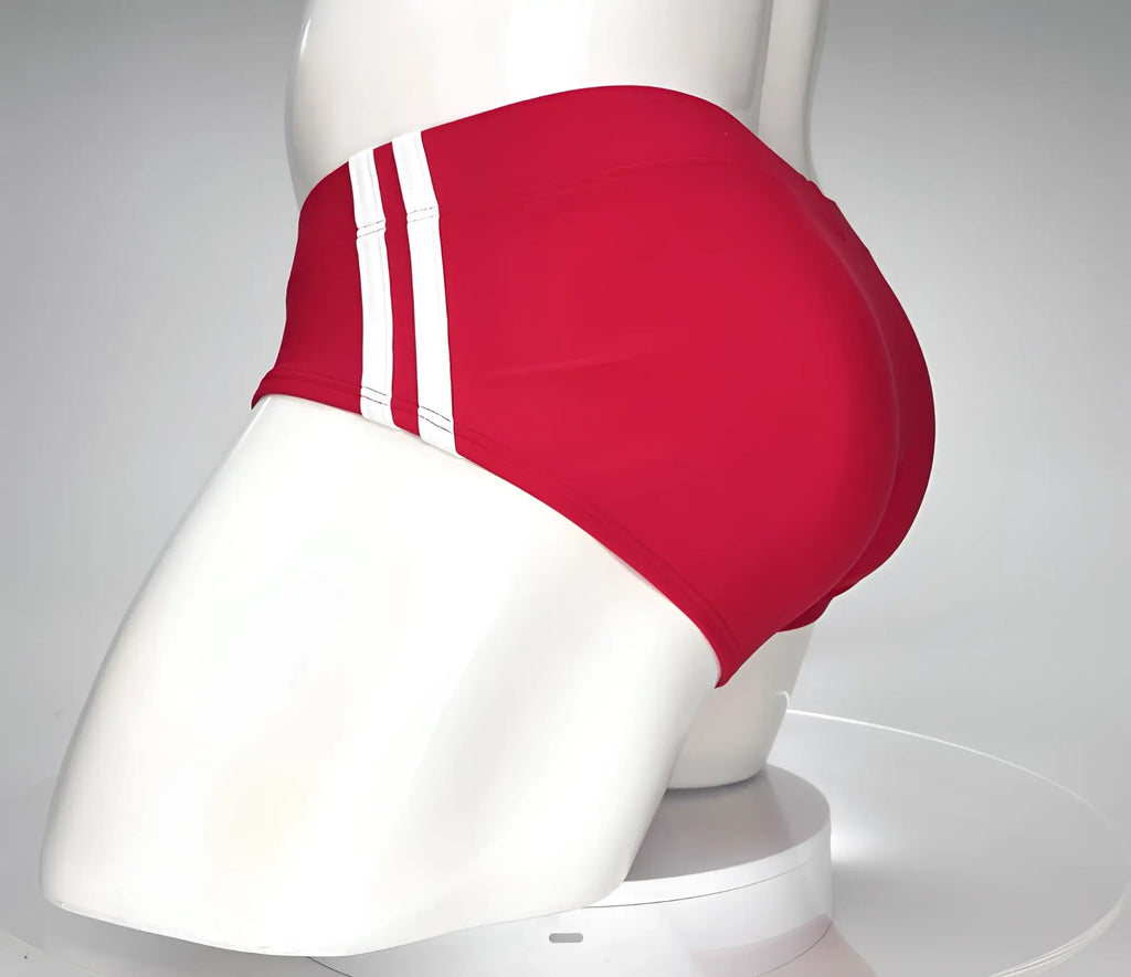 Red WildmanT swim brief on a white mannequin, featuring dual vertical white stripes on the side.