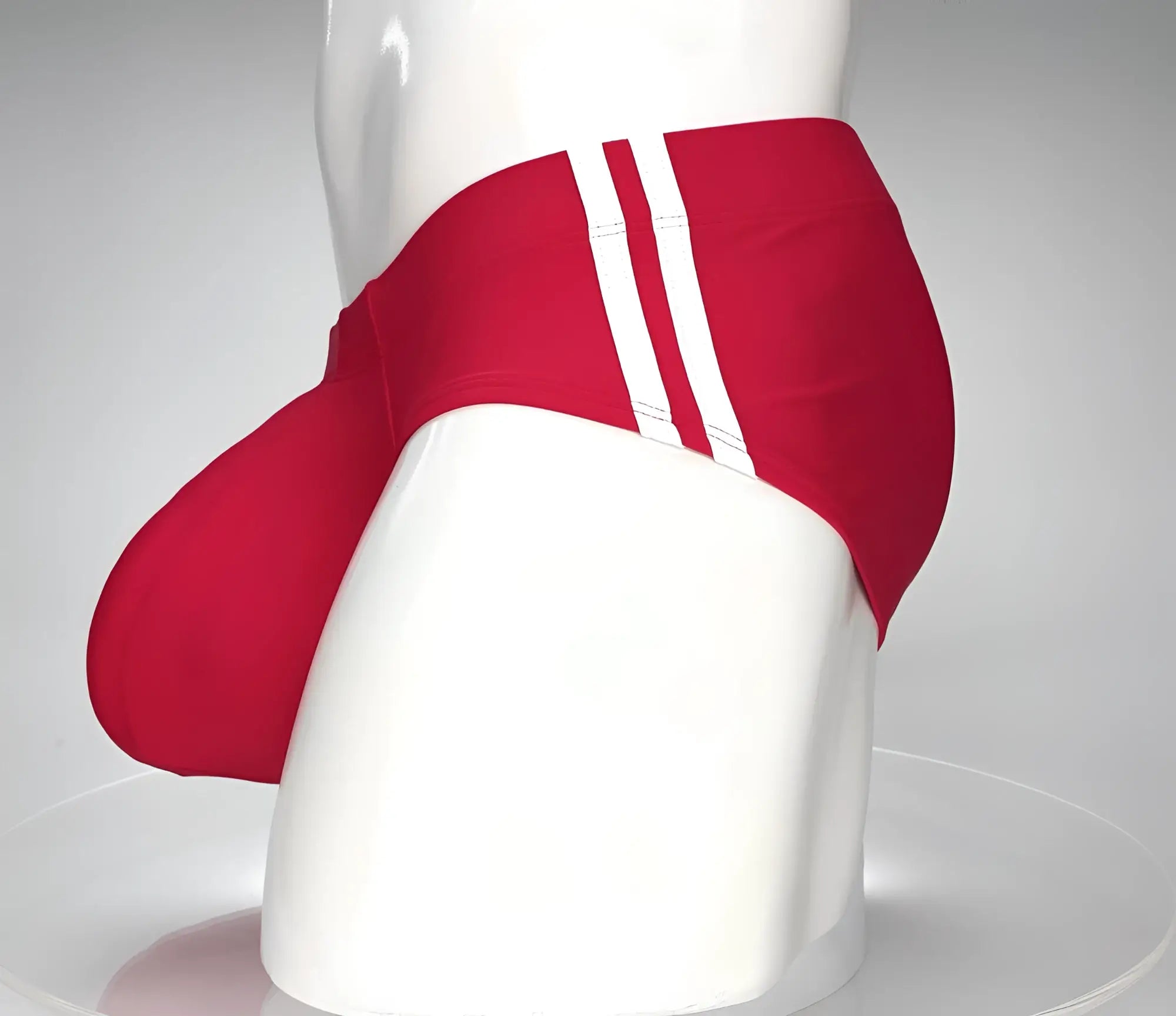 Red swim brief with prominent front pouch and dual white side stripes on a white mannequin torso.