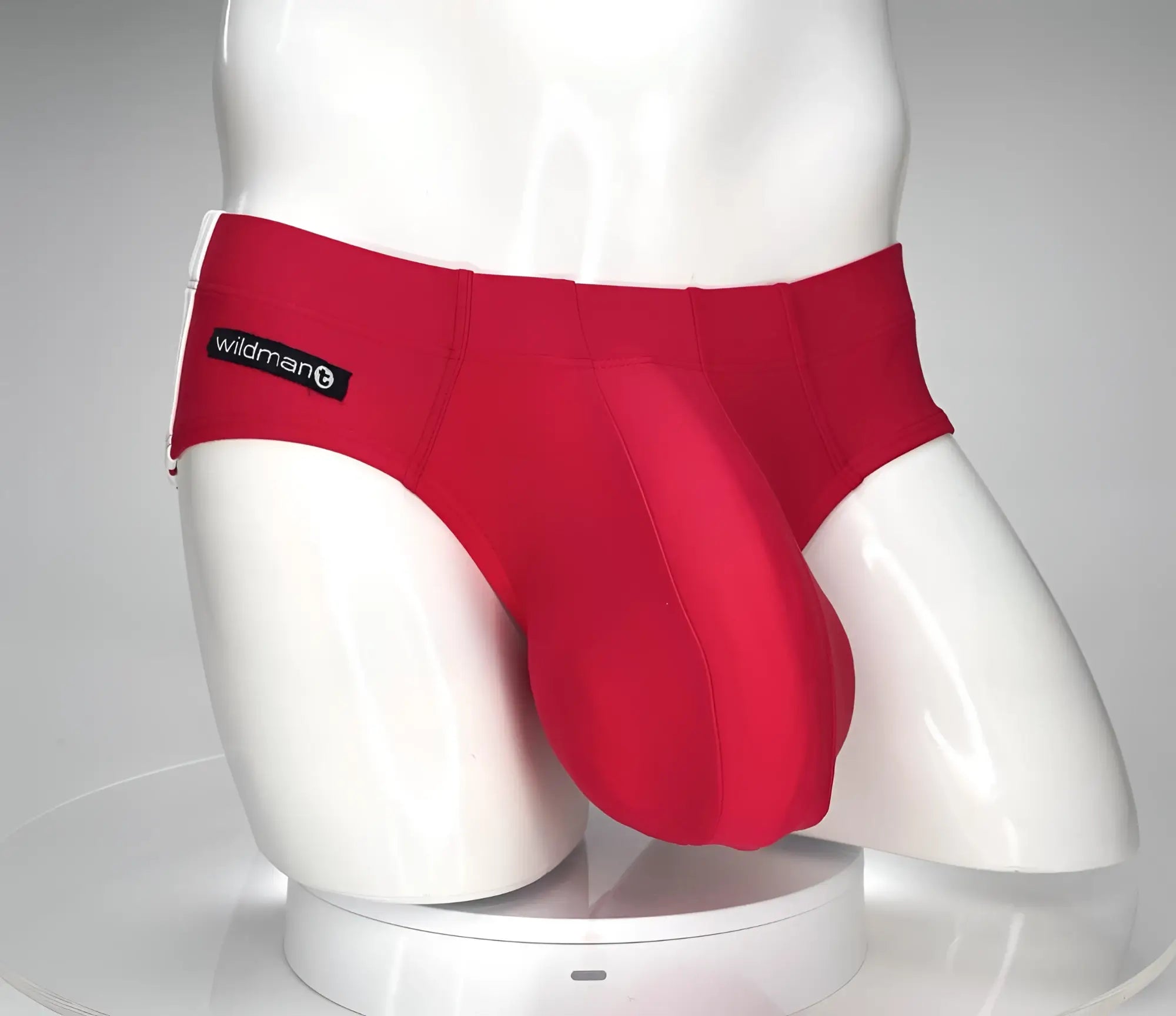 Bright red WildmanT swim brief on a white mannequin featuring a prominent, contoured front pouch and branded side tag.