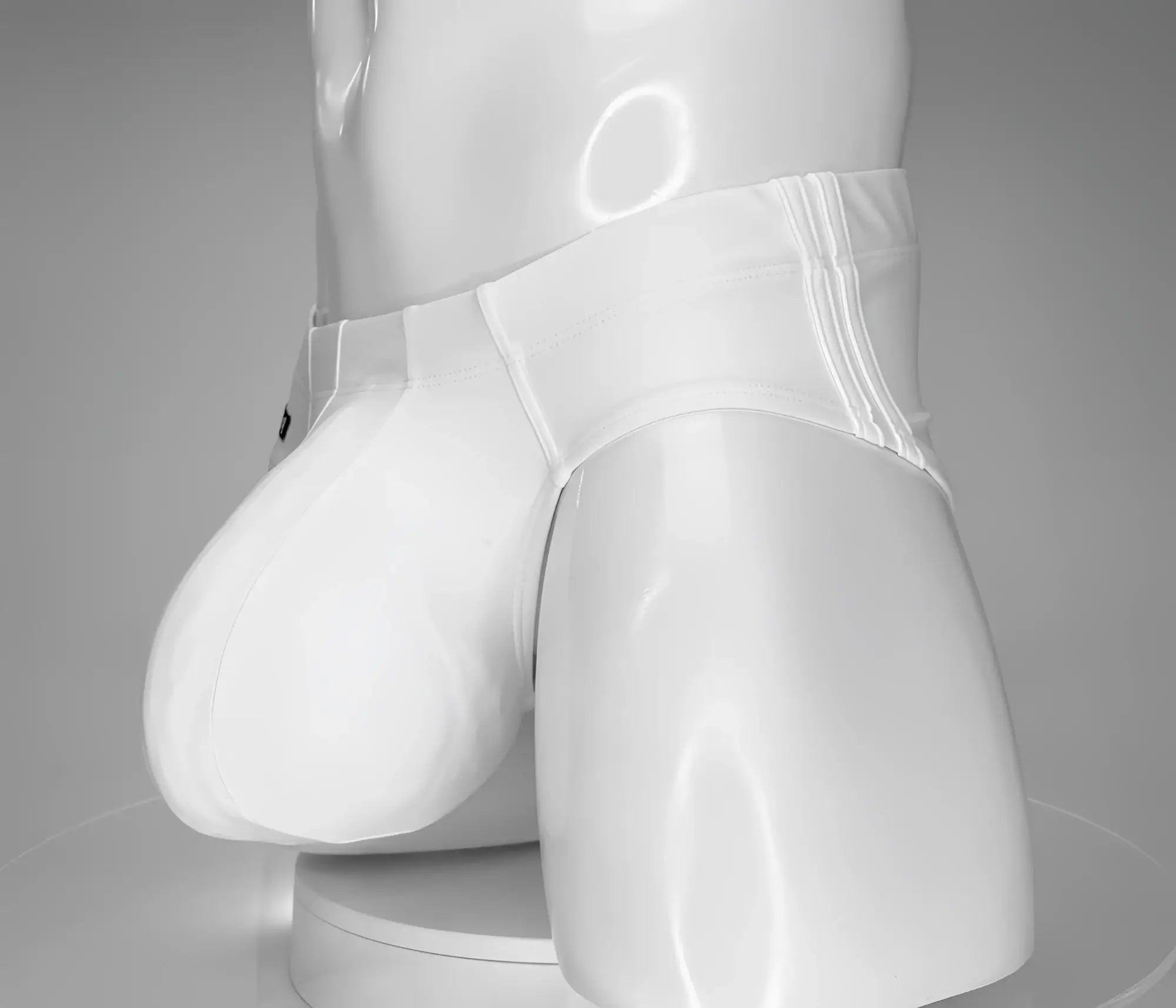 White low-rise swim brief with a large, contoured front pouch on a mannequin torso against a gray background.
