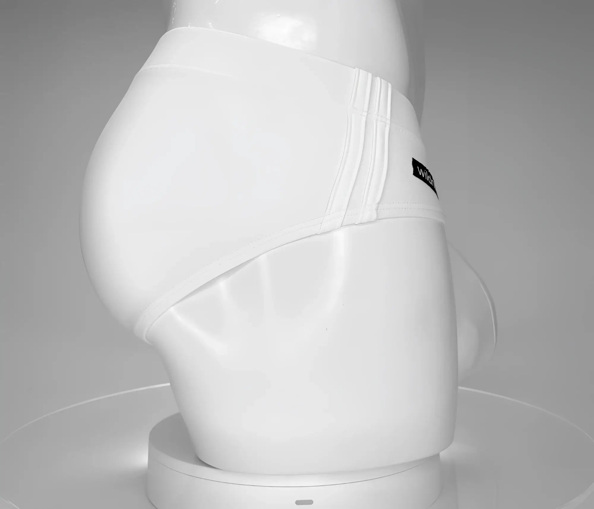 Side view of a white WildmanT swim brief on a mannequin, featuring ribbed side detailing and a small logo tag.