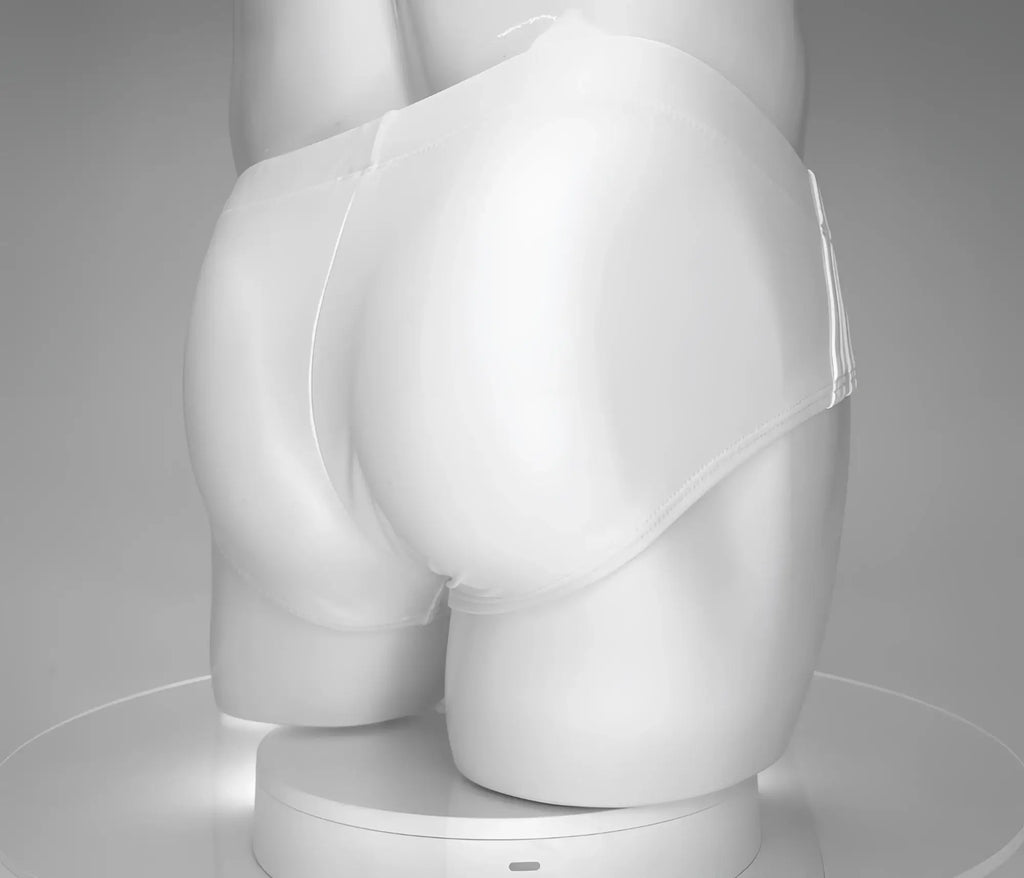 Rear view of a white, low-rise WildmanT swim brief worn by a male mannequin against a grey studio background.