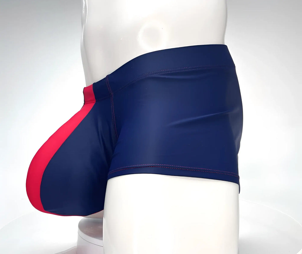 Navy blue square-cut swim trunks with a bright red front pouch and red contrast stitching on a mannequin.