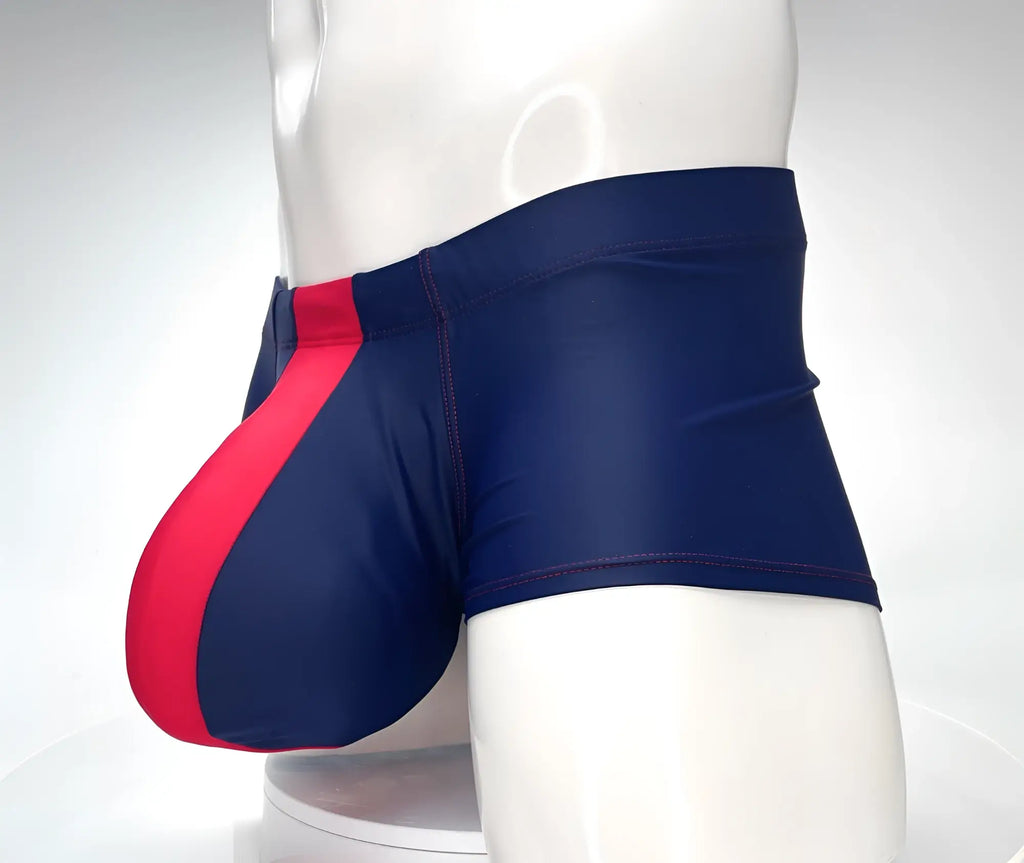 WildmanT square-cut swim trunks in navy with a red front pouch panel and red contrast stitching on a white mannequin.
