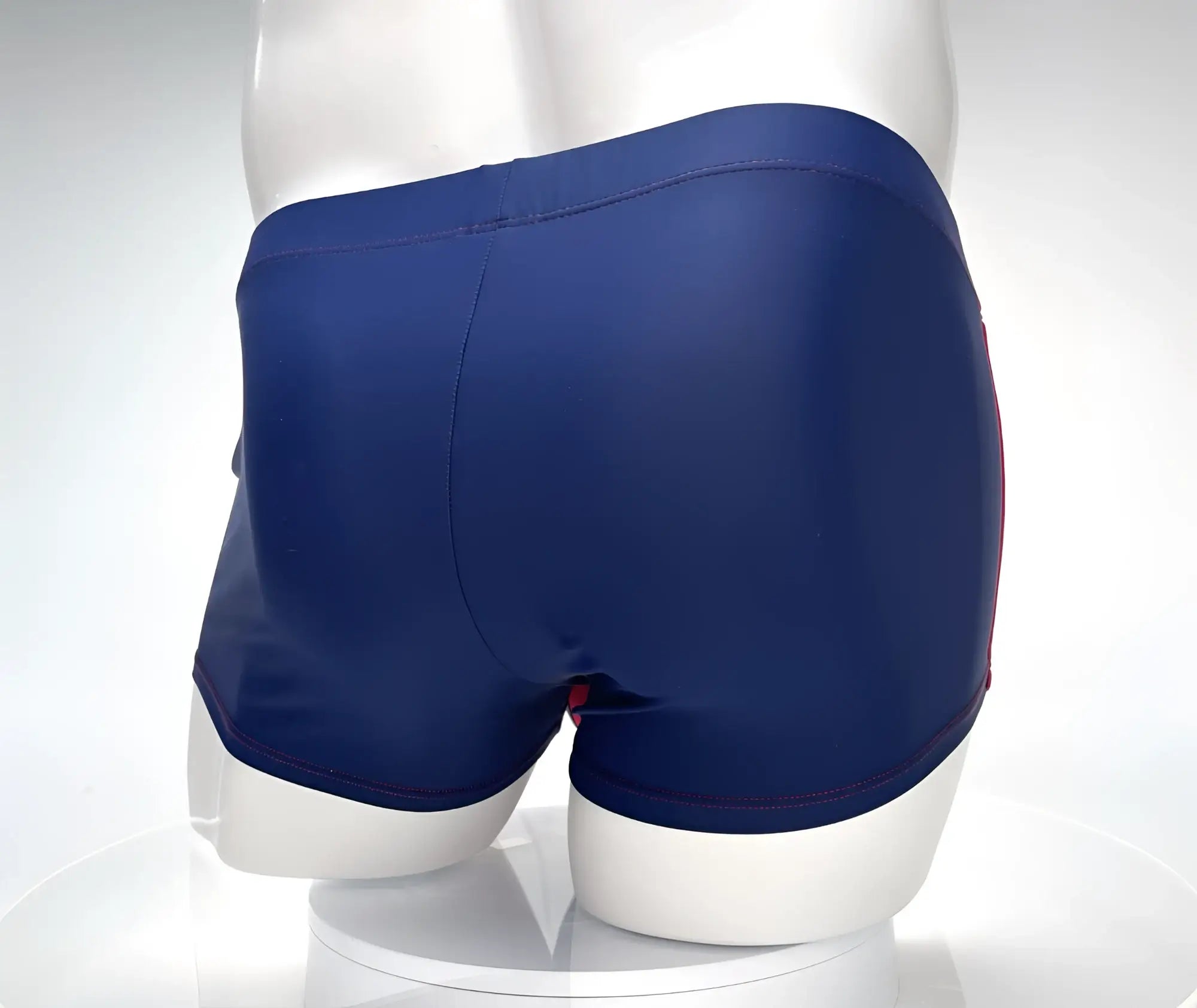 Rear view of navy blue square-cut swim trunks with red contrast stitching, shown on a white mannequin.