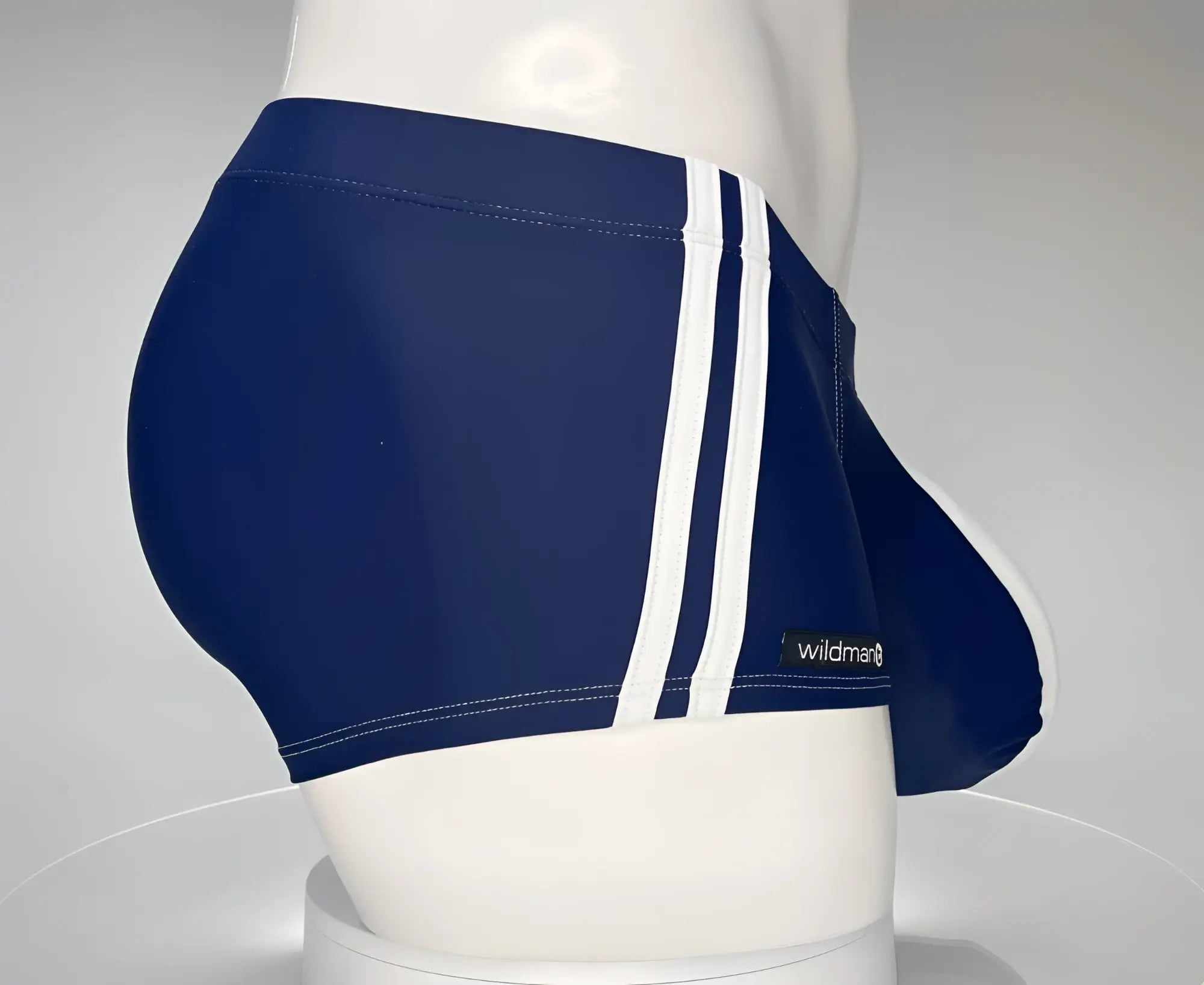 Navy blue square-cut swim trunks with white side stripes and a WildmanT logo tag on a mannequin torso.
