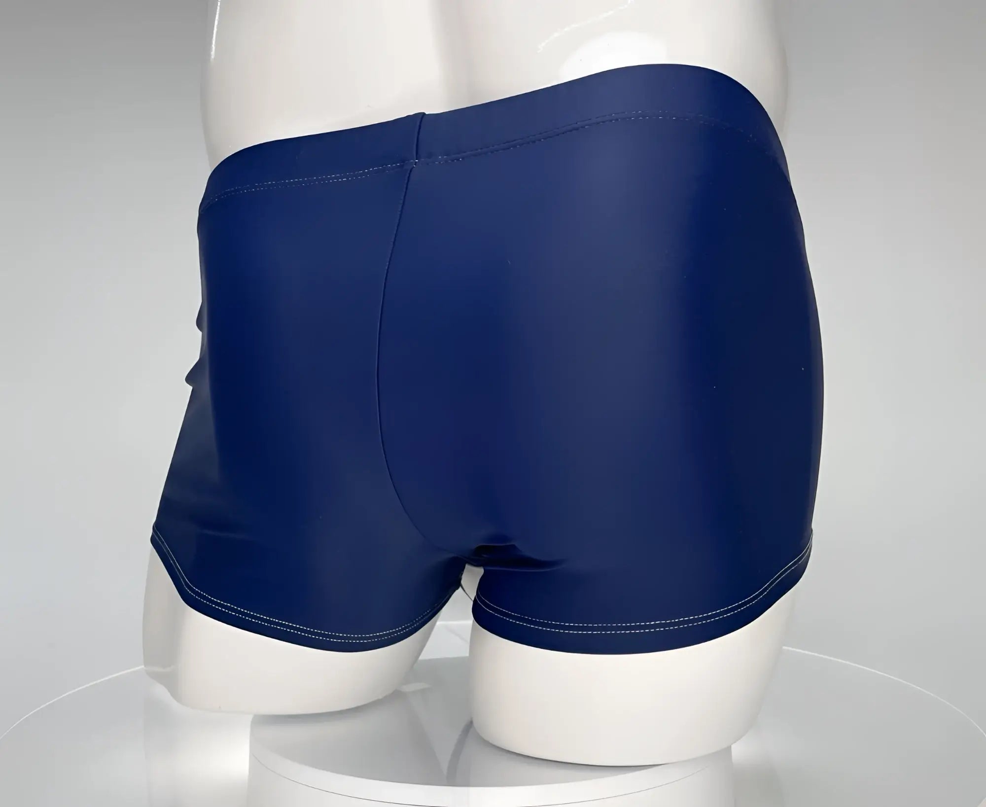 Back view of WildmanT navy blue square-cut swim trunks on a white mannequin with contrast white stitching.