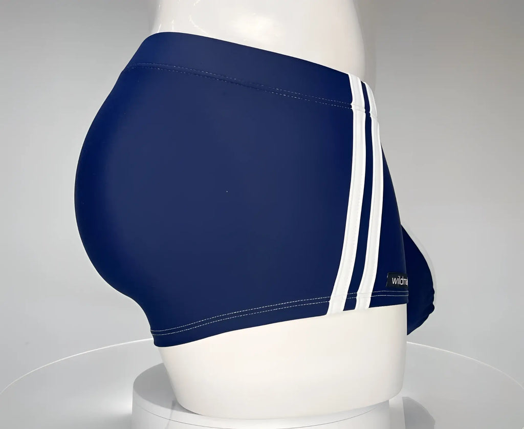 Navy blue WildmanT square cut swim trunks with dual white side stripes and a small logo tag on the hip.