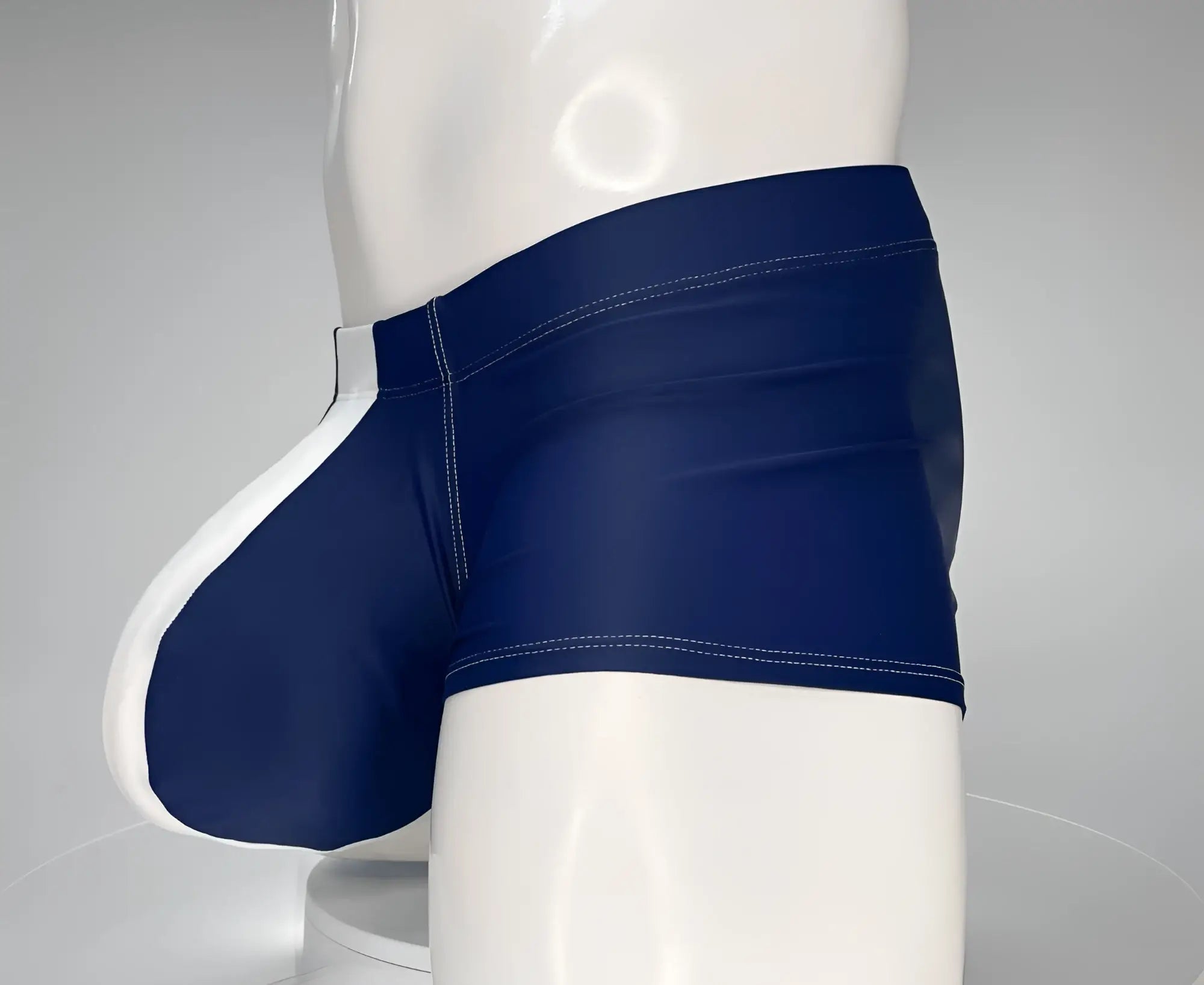 Navy blue and white square-cut swim trunks on a mannequin, featuring contrast stitching and a contoured front pouch.