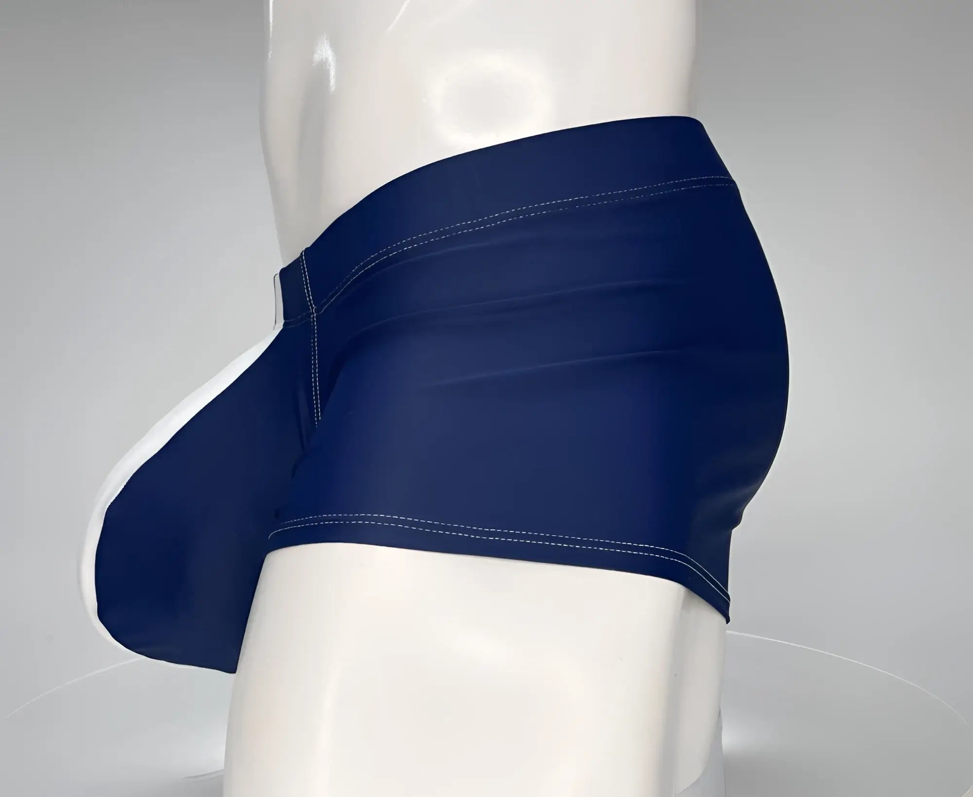 Navy and white square-cut swim trunks on a mannequin, featuring a contoured front pouch with white contrast piping.