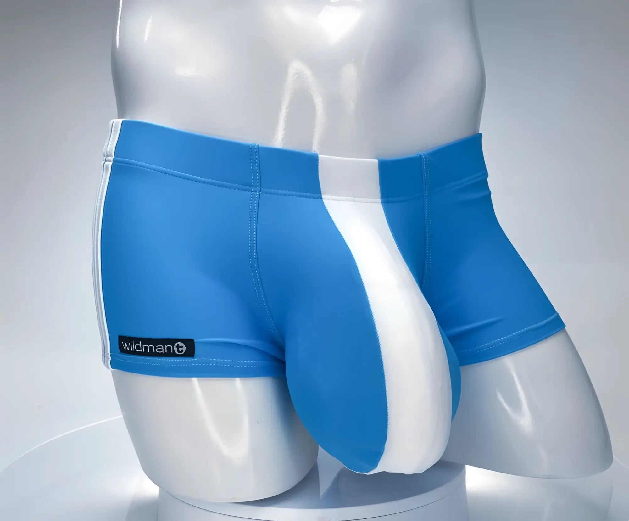 Teal and white WildmanT square-cut swim trunks on a mannequin, featuring a prominent contoured front pouch.