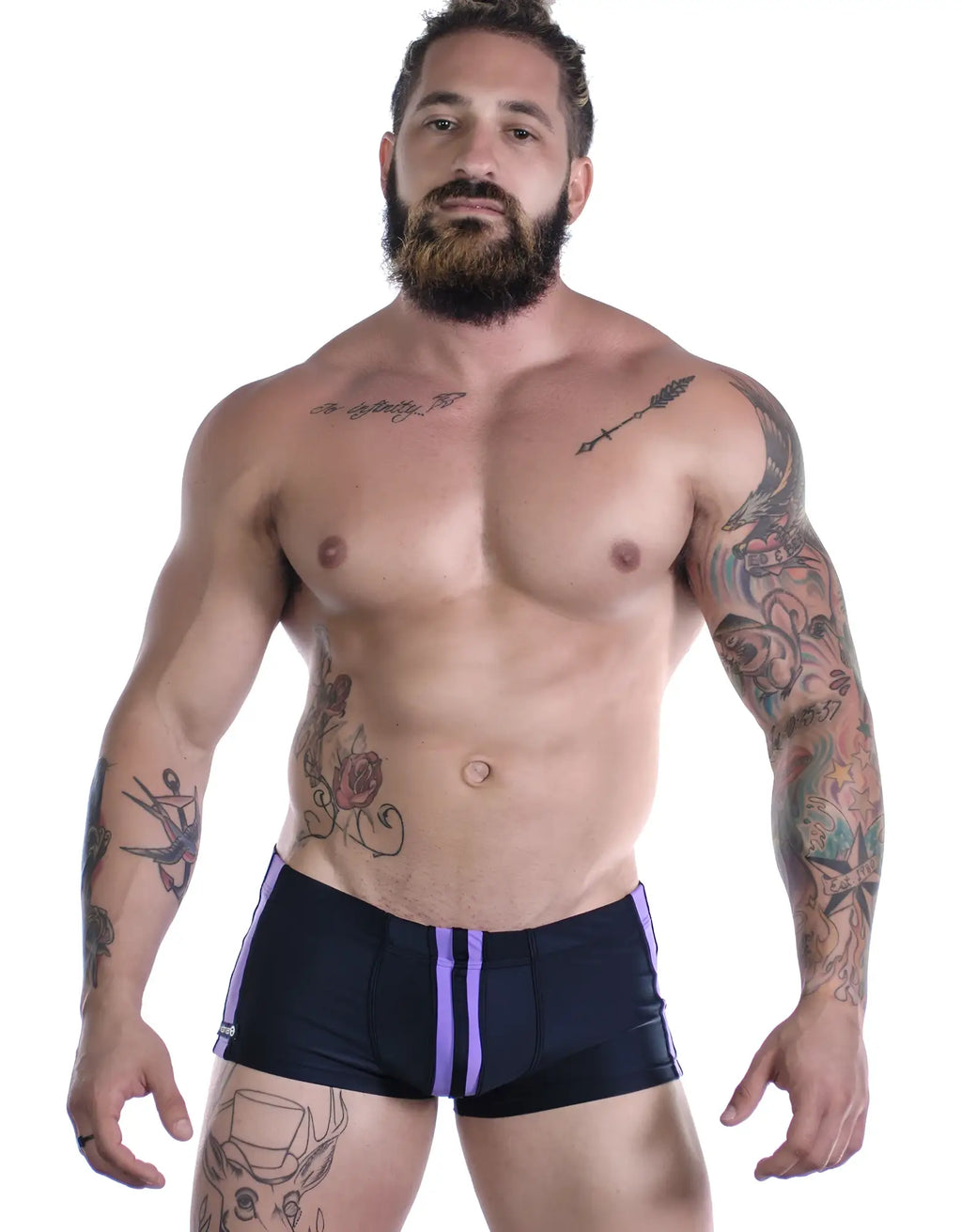 Sportivo square cut trunks in black with dual purple side stripes, modeled by a muscular, tattooed man.