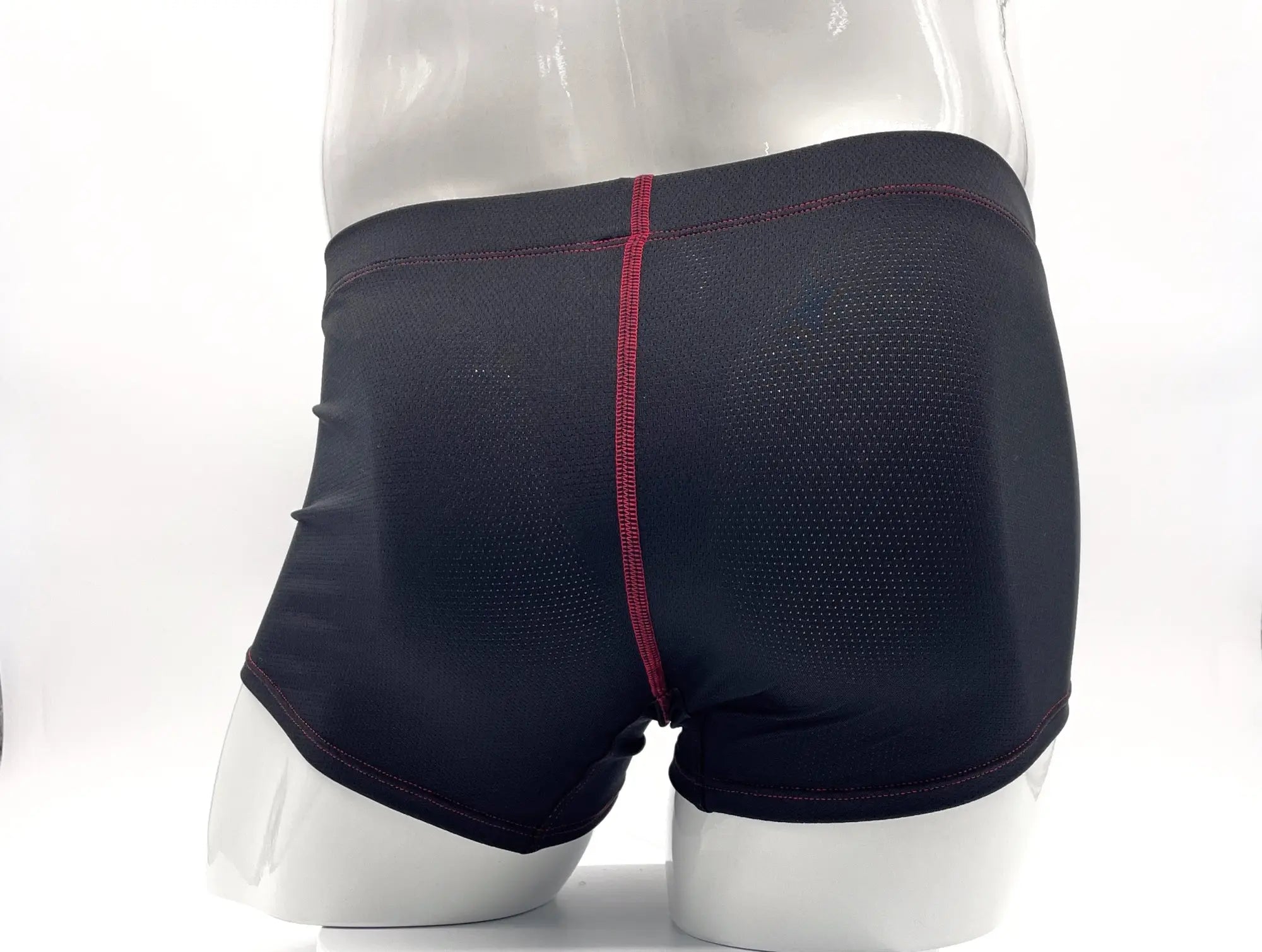 Black mesh boxer briefs on a mannequin with red contrast stitching down the center and along the hems.