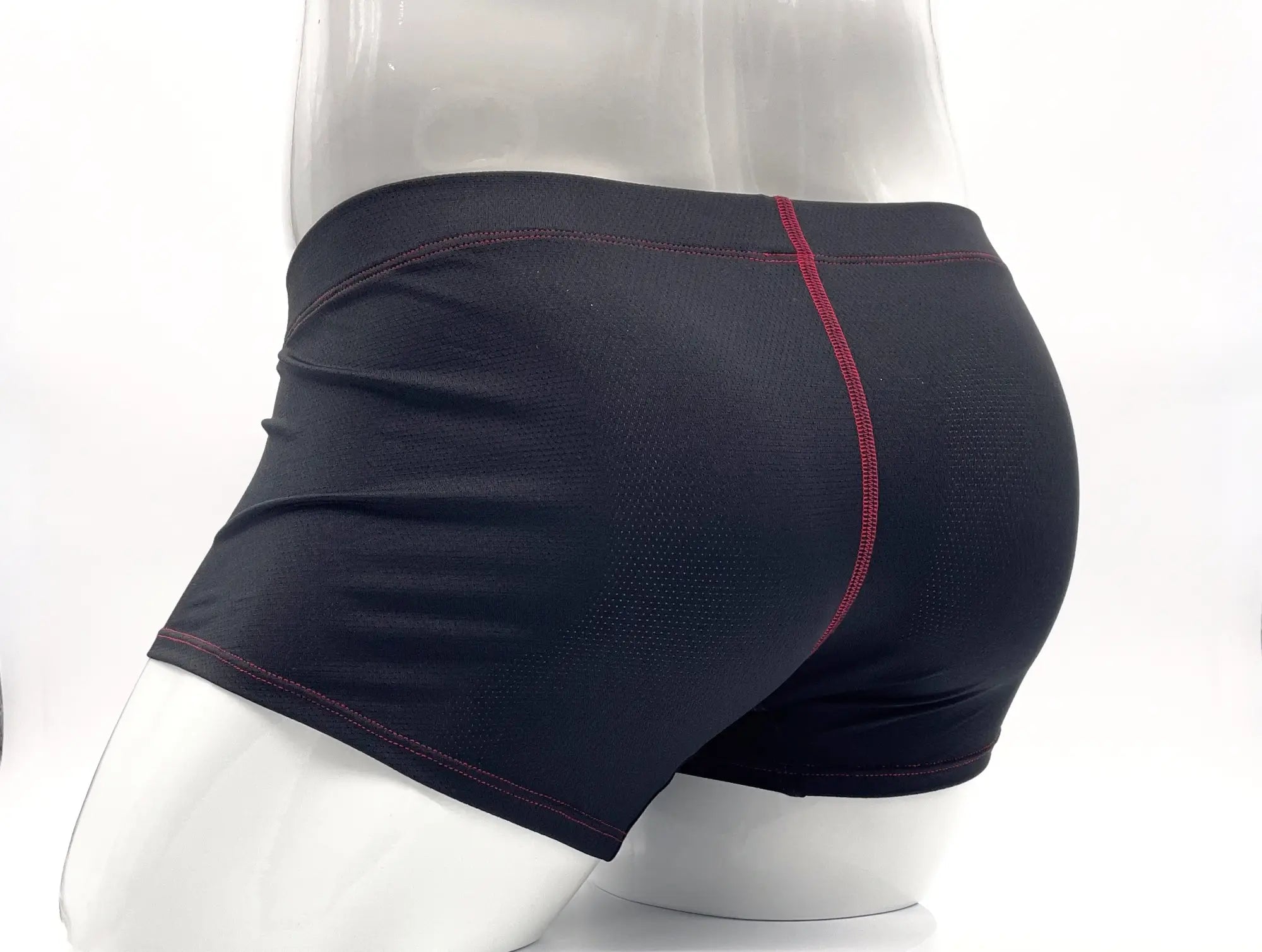 Black perforated boxer briefs on a mannequin with red contrast stitching at the seams.
