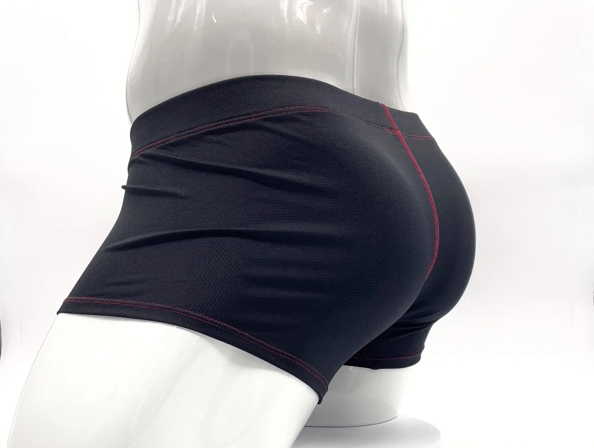 Black boxer briefs on a mannequin, featuring textured fabric and decorative red contrast stitching on seams.