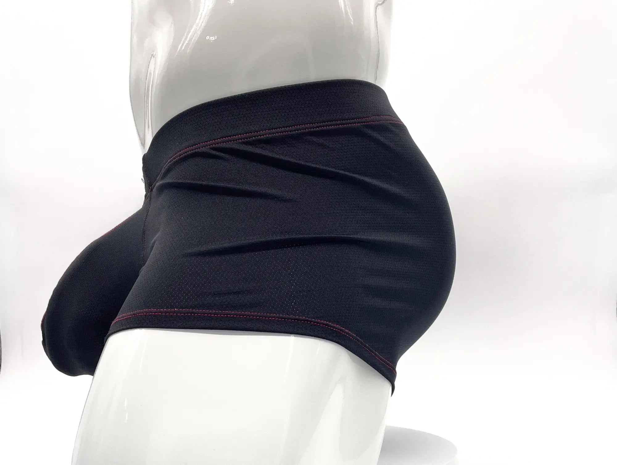 Black boxer briefs with a prominent pouch, textured fabric, and red contrast stitching worn on a white mannequin.