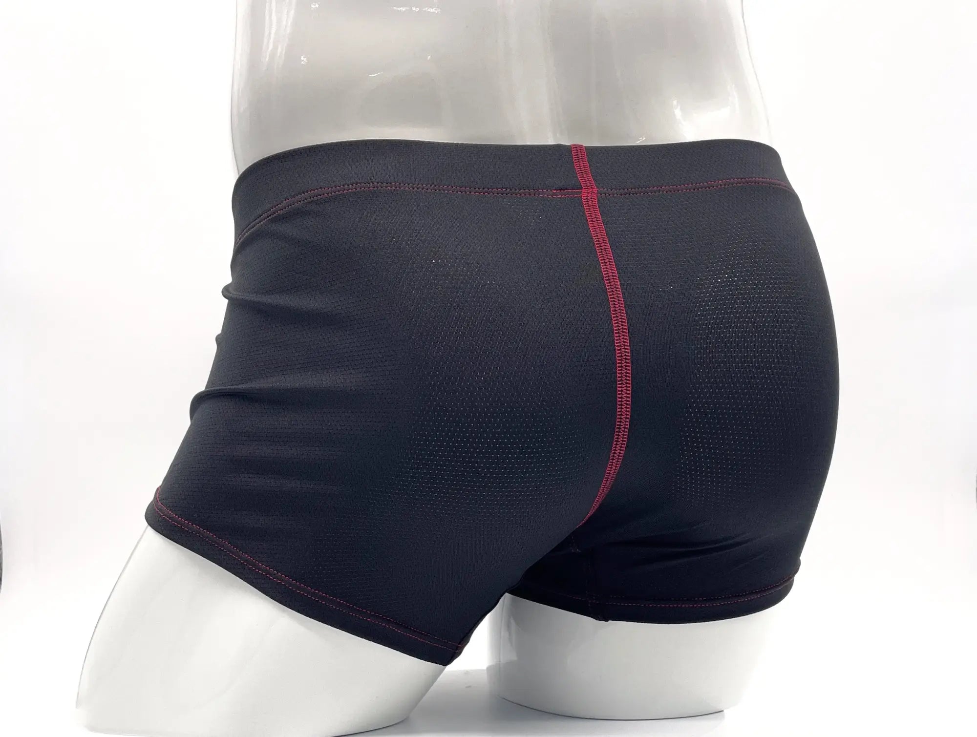Black boxer briefs on a mannequin, featuring textured fabric and prominent red stitching details along the seams.