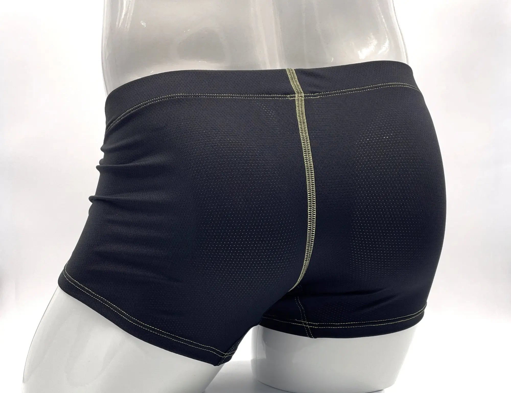 Black mesh boxer briefs on a mannequin, featuring prominent yellow contrast stitching along the back seam and hems.