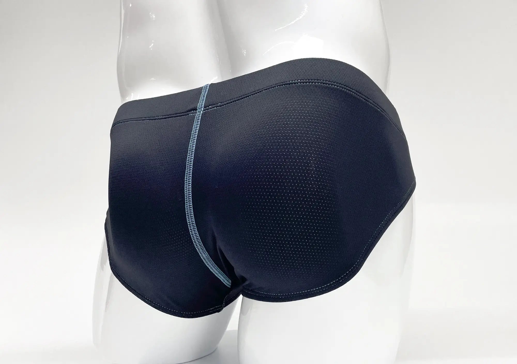 Back view of blue perforated fabric pouch briefs on a white mannequin with a prominent light blue center seam.