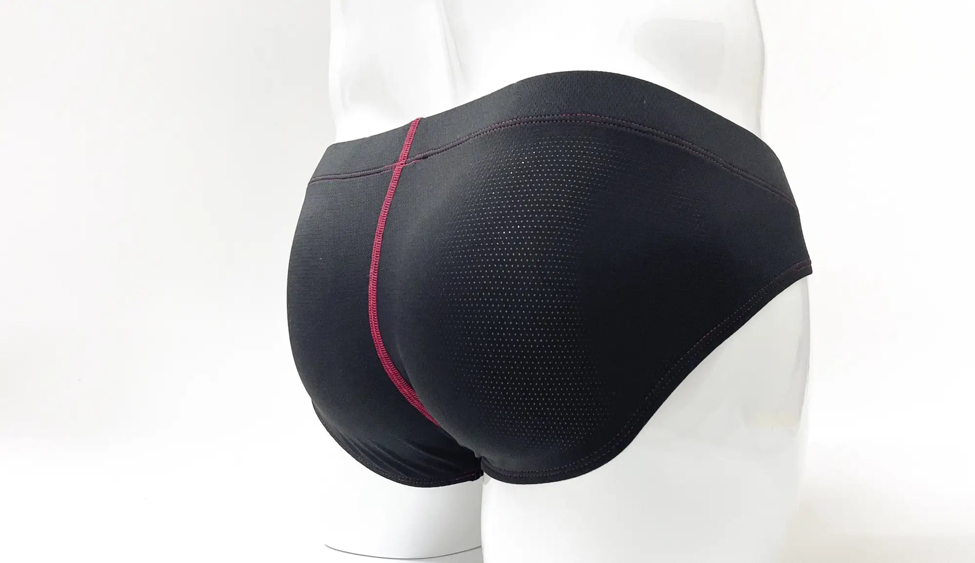 Black perforated pouch brief with red contrast stitching, shown from the rear on a mannequin.