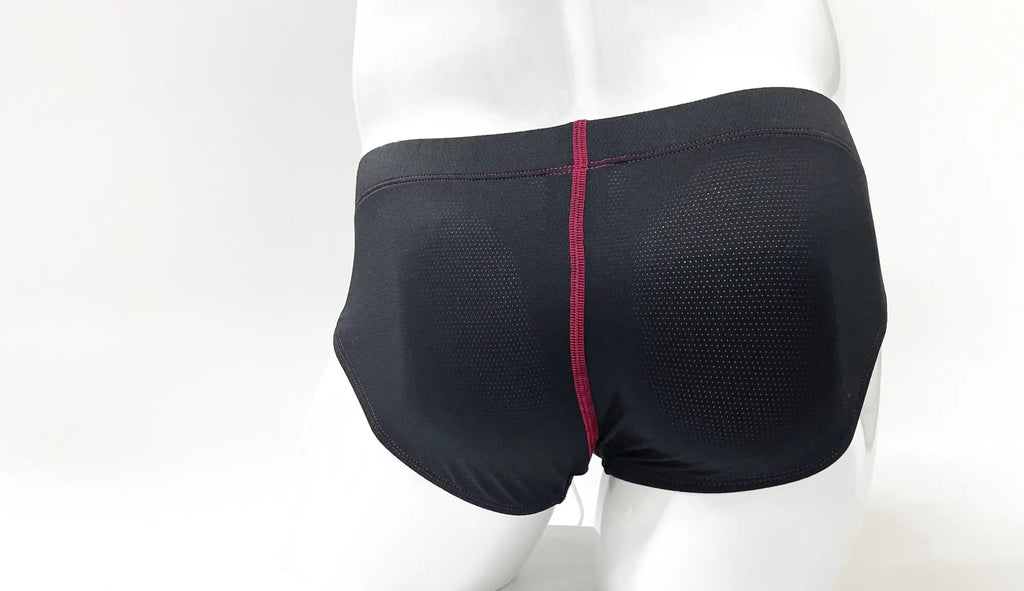 Black perforated fabric men's brief with a prominent vertical red center seam on a mannequin torso.