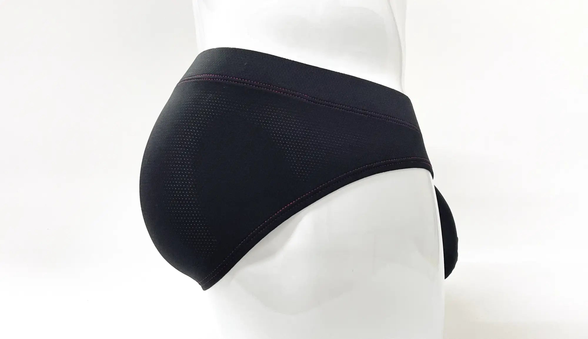 Black pouch brief on a mannequin, featuring perforated fabric and red stitch detailing along the waistband and seams.