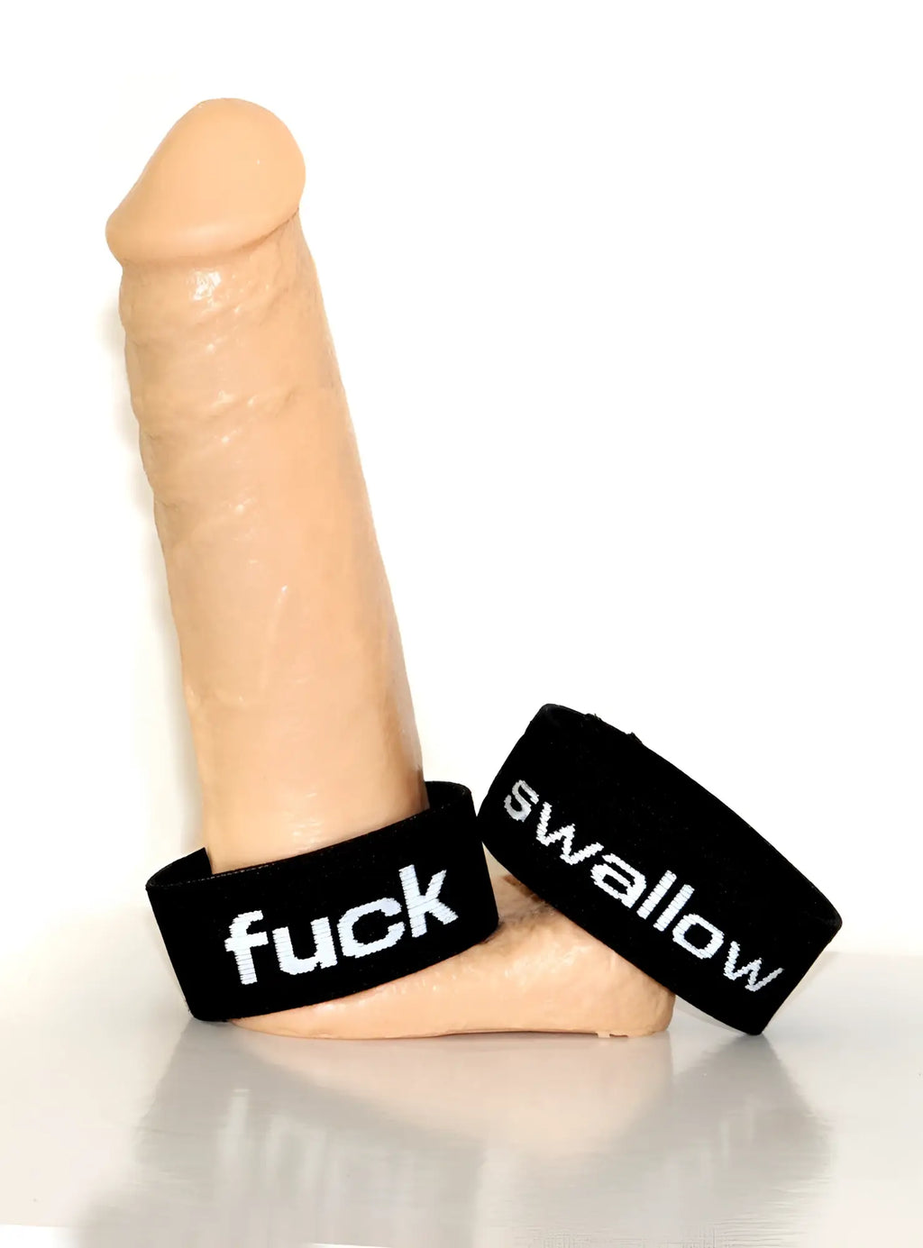 Flesh-toned phallus display base featuring two black elastic rings with white embroidered text "fuck" and "swallow".